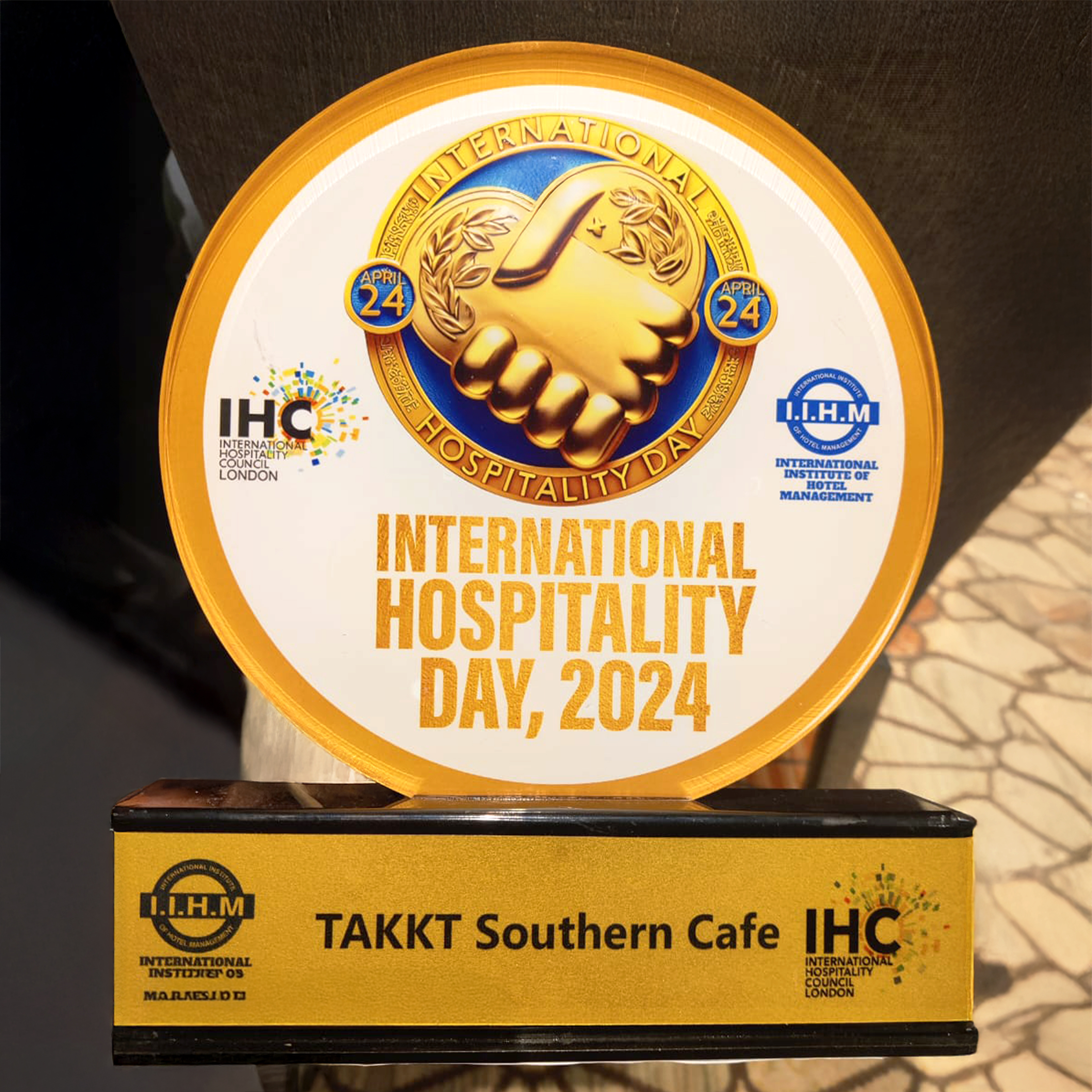 Award plaque for International Hospitality Day 2024 featuring a golden handshake emblem and the date April 24, presented to TAKKT Southern Cafe.