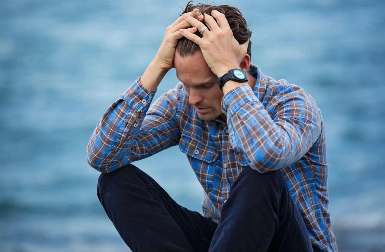 Homme assis la tête dans les mains, illustrant la détresse face aux effets secondaires des médicaments antiépileptiques.