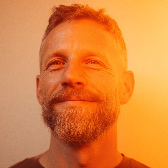 Smiling middle-aged man with short hair and a beard bathed in warm orange light.