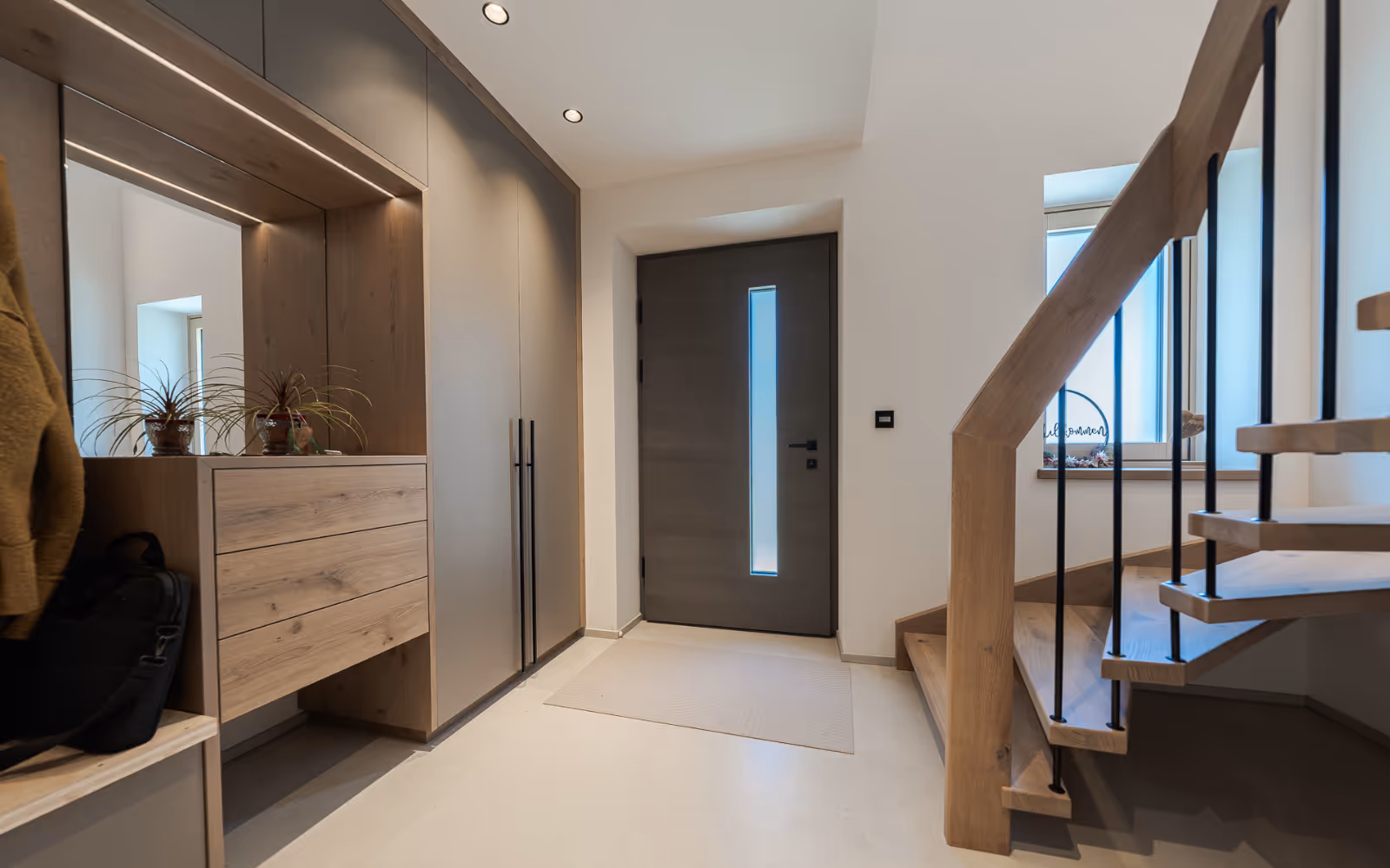 Moderner Eingangsbereich mit Holztür, integriertem Garderobenschrank und Treppe mit Holzgeländer.