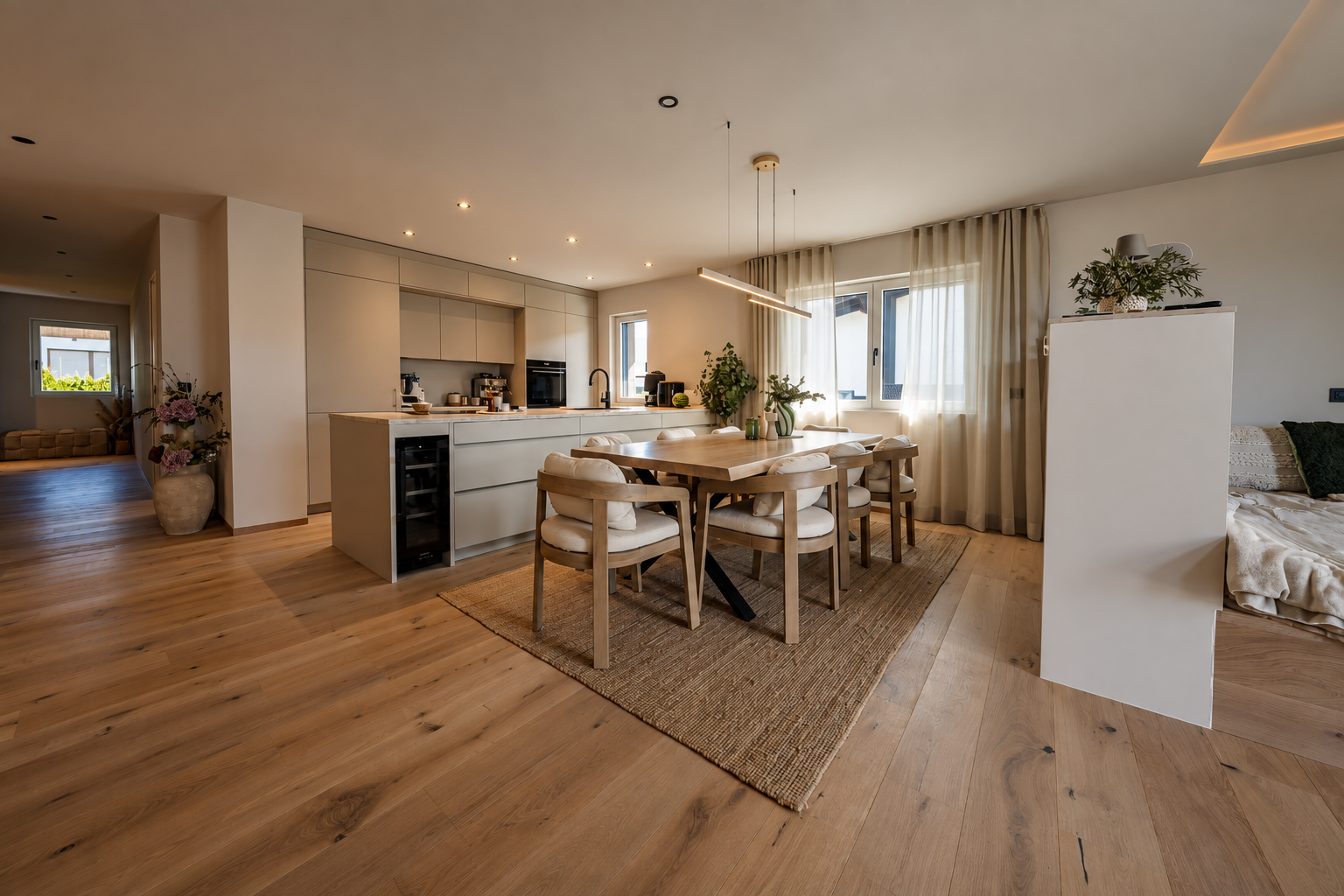 Modernes Wohnzimmer mit großer Creme-eckcouch, Holzbalkendecke, Fernseher, Pflanzen und großen Fenstern mit Blick auf eine Terrasse und grüne Berge.