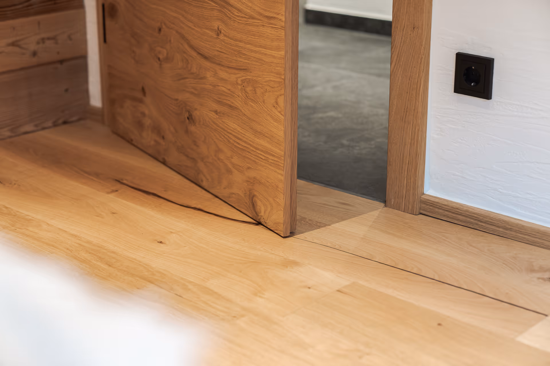 Detailaufnahme einer maßgefertigten Holztüre von SR.Schauraum, harmonisch kombiniert mit einem hochwertigen Echtholzboden. Die natürliche Maserung, präzisen Übergänge und warmen Materialien zeigen die handwerkliche Qualität und das stilvolle Wohnkonzept.