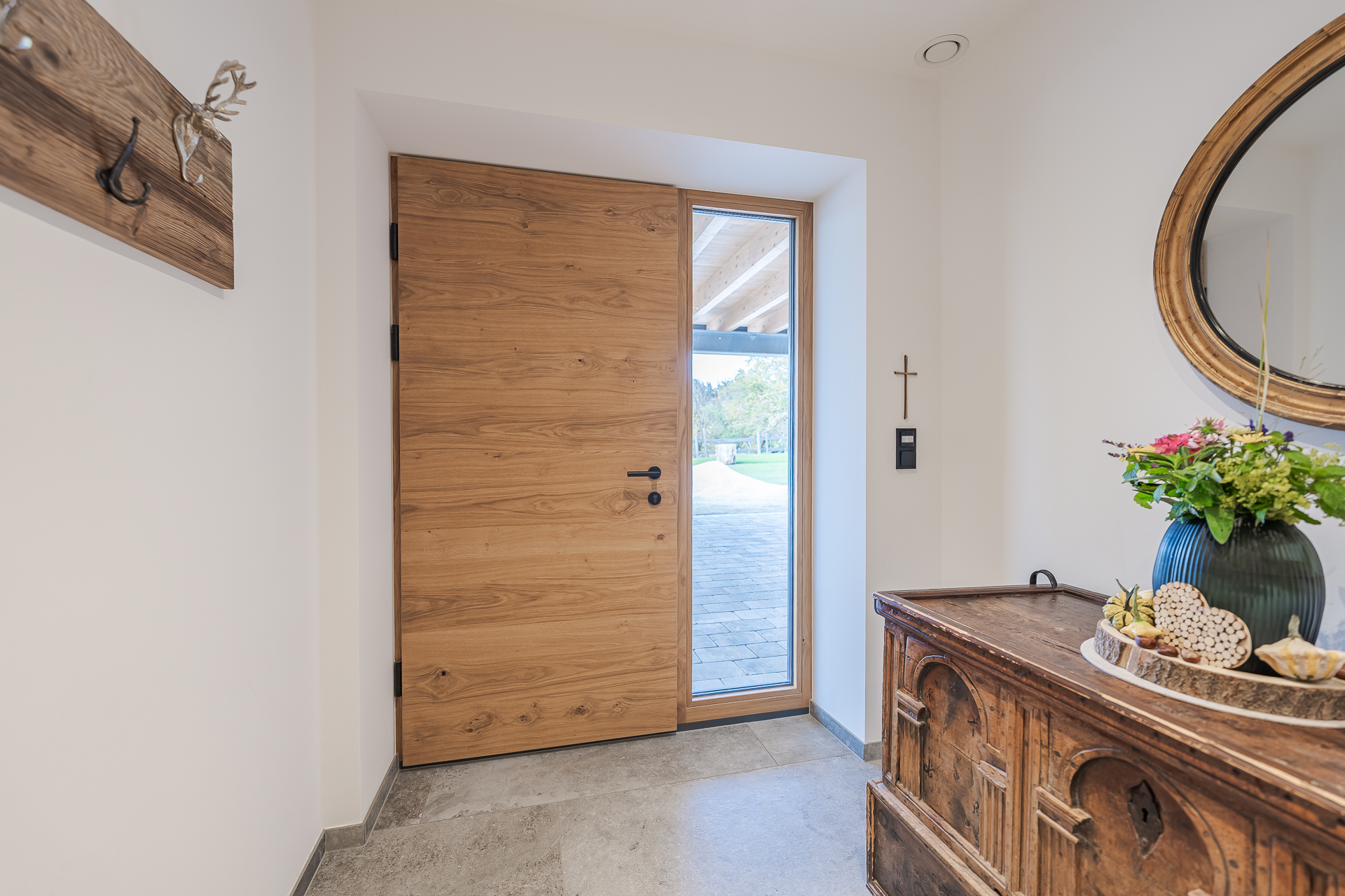 Eingangsbereich mit moderner Massivholz-Haustür und seitlichem Glaslicht. Der warme Holzton kombiniert sich harmonisch mit der hellen Wandgestaltung und dem rustikalen Sideboard, wodurch ein einladendes und stilvolles Ambiente entsteht.