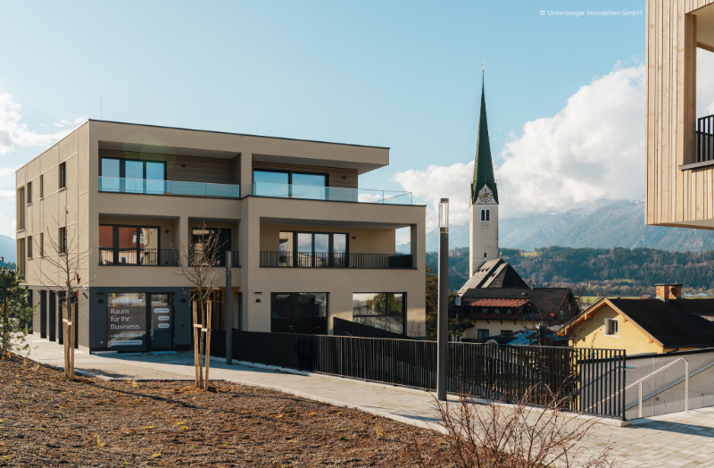 Modernes Mehrparteienhaus in Kirchberg in Tirol mit großzügigen Balkonen, hochwertigen Fenstern und Blick auf die Pfarrkirche sowie die Tiroler Berglandschaft.