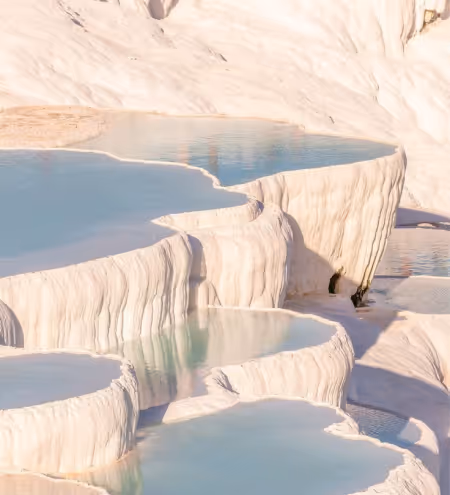Natural terraced pools filled with clear blue water against white mineral deposits at a cliffside.