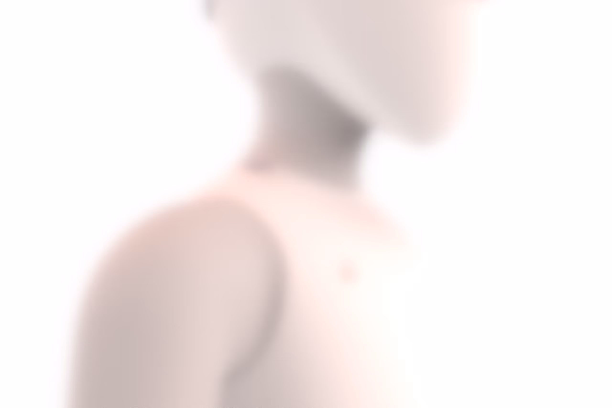 Blurred close-up of a person's neck and shoulder with soft lighting on a white background.