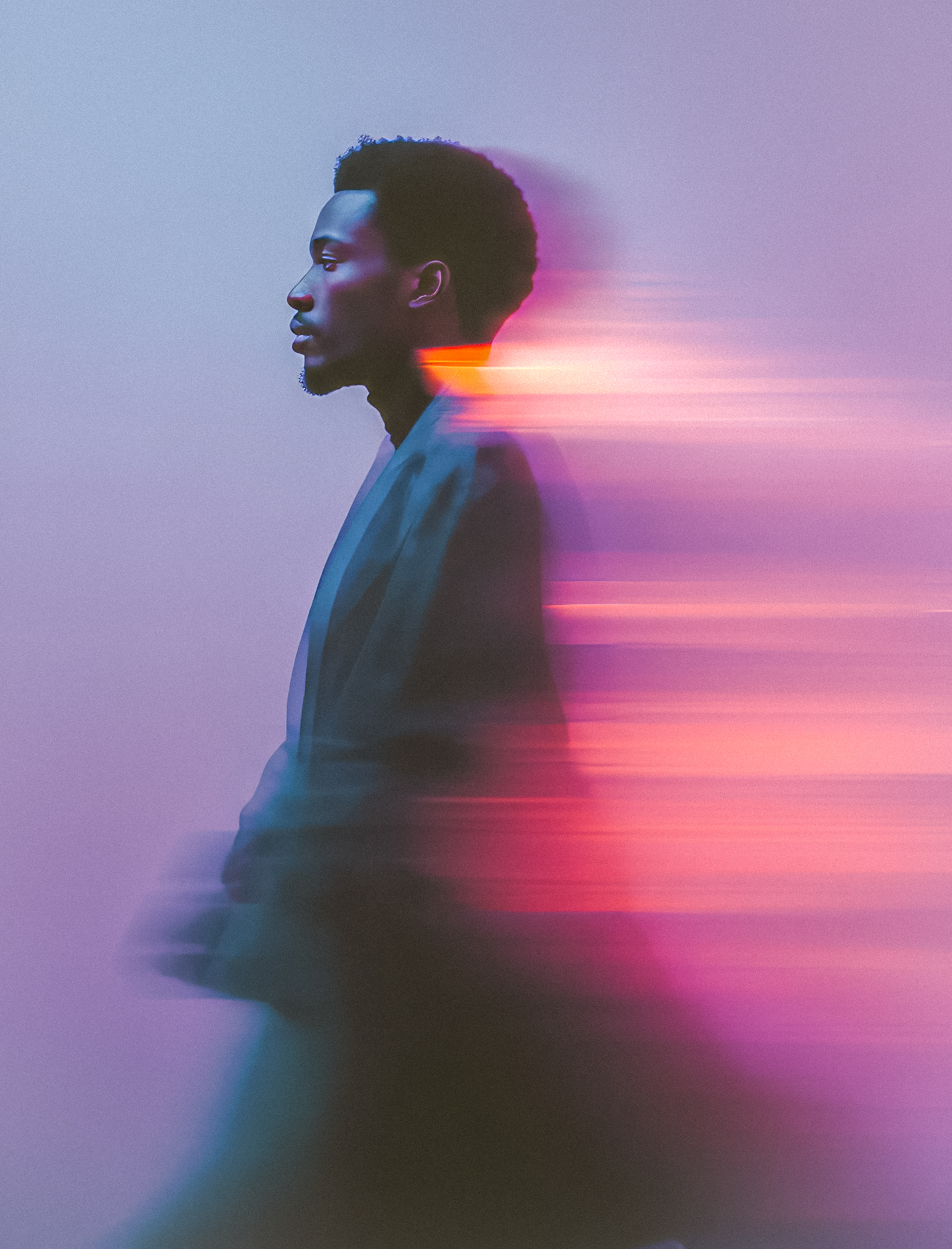 Side profile of a man with an afro hairstyle and beard, with motion blur and pink and purple light trails behind him.