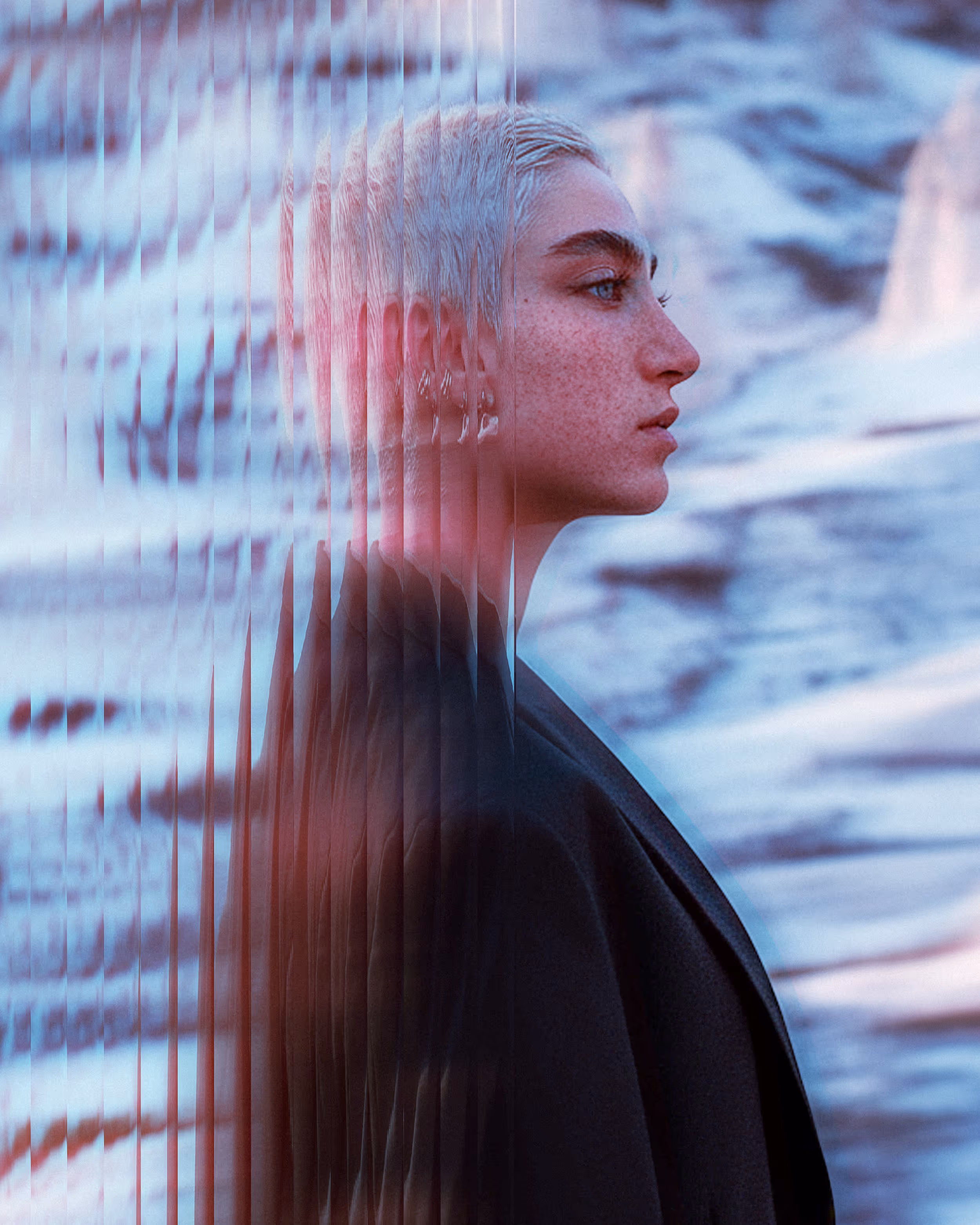Profile of a person with short light hair and freckles wearing a dark coat, with a distorted glass effect splitting the image vertically.