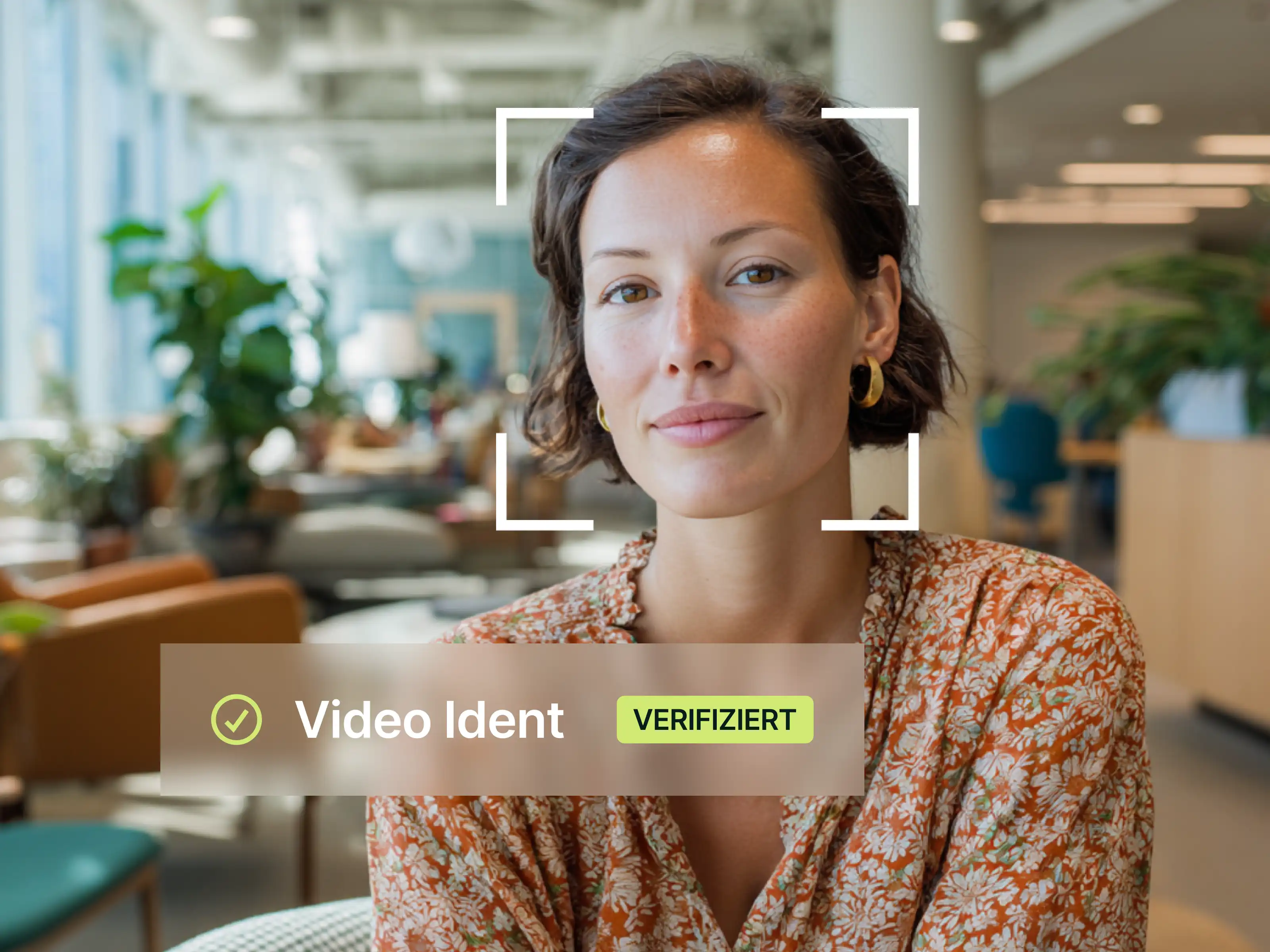 Junge Frau mit kurzen braunen Haaren und goldenen Ohrringen trägt ein geblümtes orangefarbenes Hemd in einem modernen, gut beleuchteten Büro mit Pflanzen im Hintergrund.