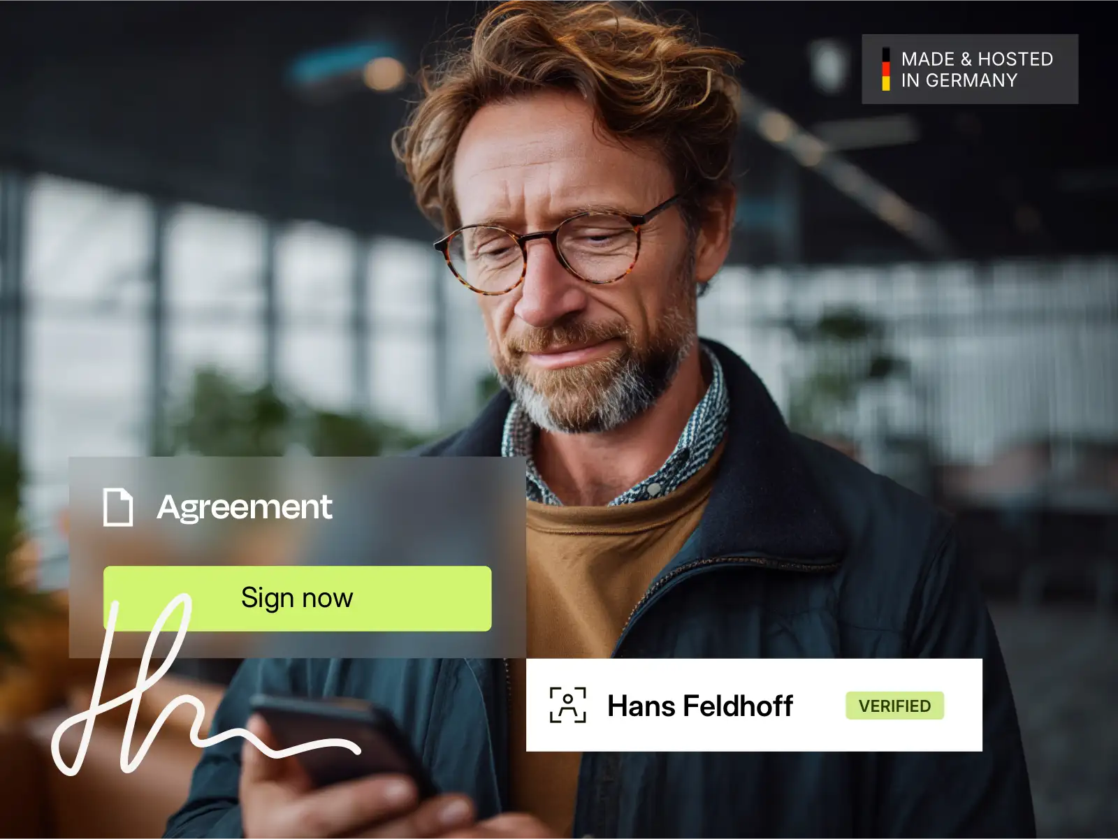 Man wearing glasses holds a smartphone and digitally signs a document called an agreement with a verified identity.