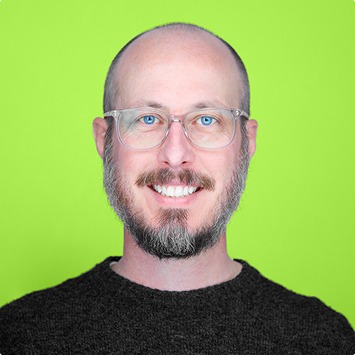 Portrait of a man in a white shirt, facing forward and smiling slightly, set against a plain white background.