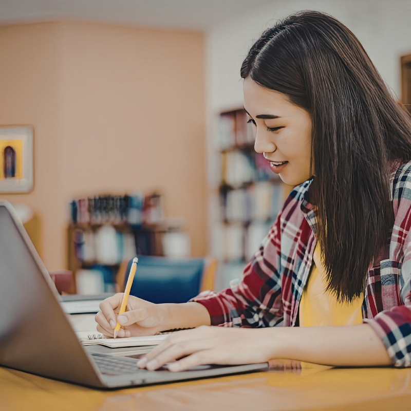 A young person smiling while writing at a desk