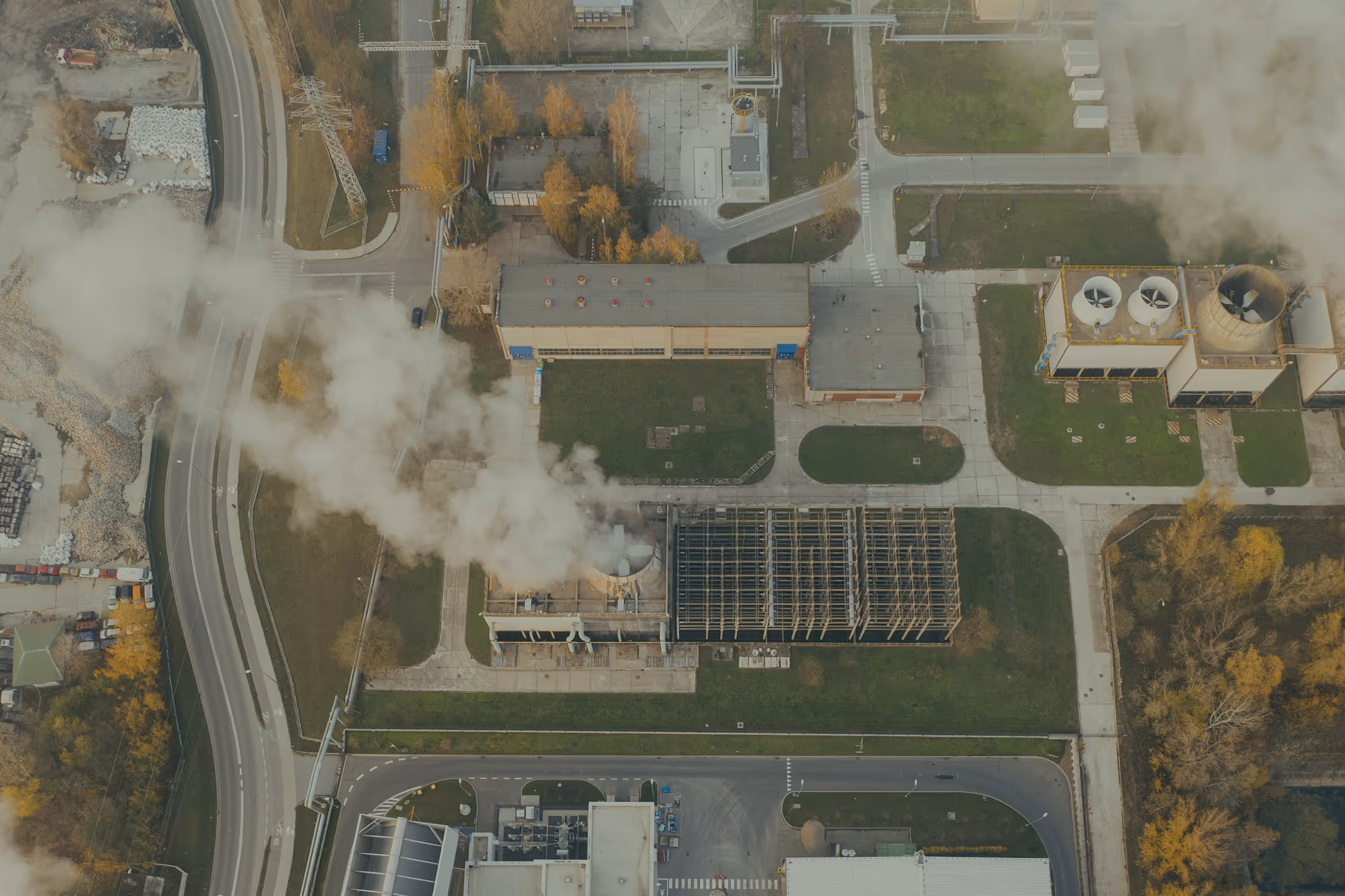 Aerial view of a critical infrastructure facility emitting smoke, illustrating vulnerability to physical and cyber threats due to outdated inspection methods, fragmented data, and rising regulatory demands — highlighting the need for autonomous drone monitoring, AI-powered anomaly detection, and secure data solutions for power plants and utility operators.