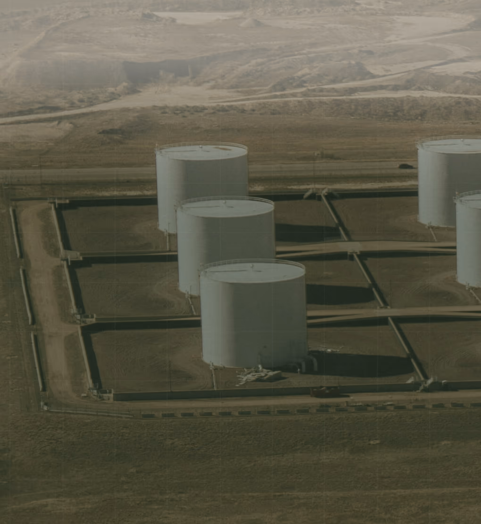 Large fuel storage tanks in a secured desert facility, representing encrypted communication and compliance-driven cybersecurity for critical energy and utility infrastructure.