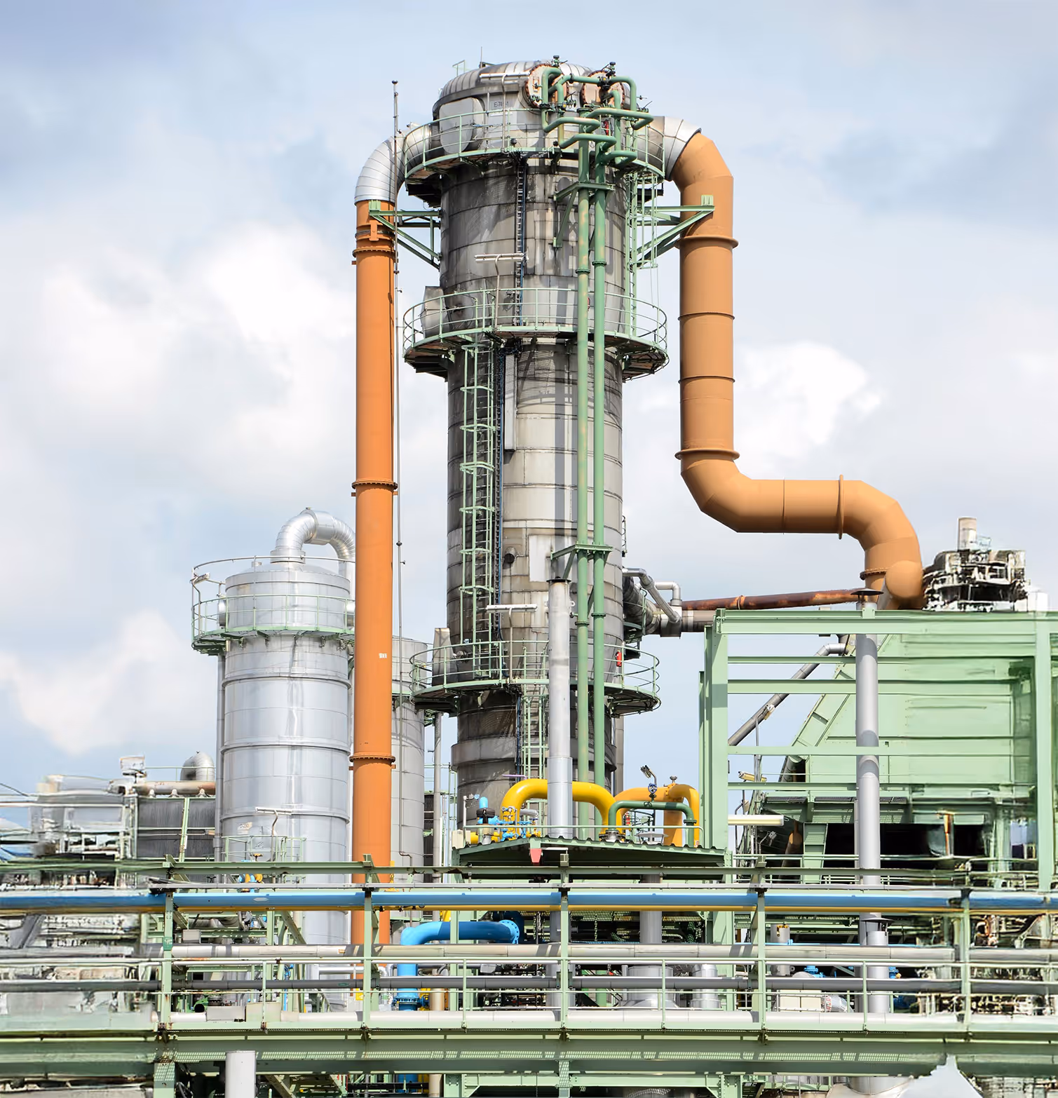 Industrial pipeline and energy distribution facility with large processing towers, orange ducts, and interconnected pipes, representing infrastructure monitoring and operational security for the oil, gas, and energy distribution sector.