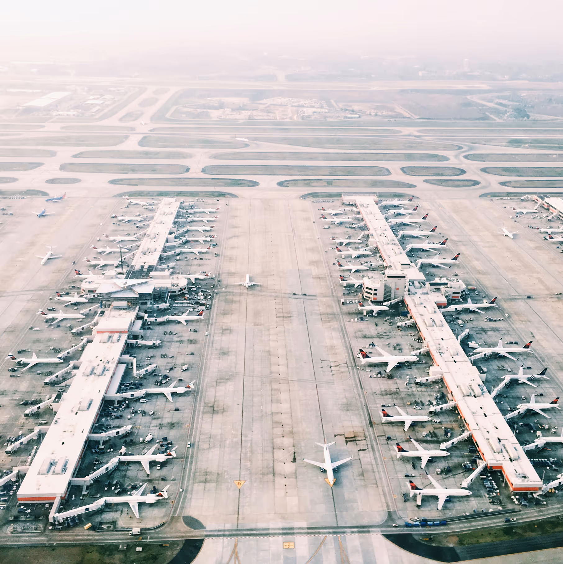Aerial view of a large international airport with multiple runways, taxiways, and terminal gates filled with commercial aircraft, representing transportation infrastructure and public works facilities.