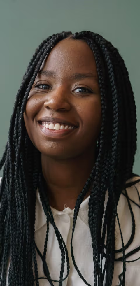 Portrait of a smiling woman with long box braids, wearing a white top, against a muted green background