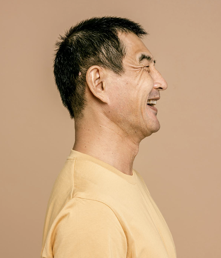 A person with short, dark hair is shown in a side profile against a plain, beige background. They are wearing a light beige, round-neck shirt and appear to be in a calm, neutral setting with soft lighting.