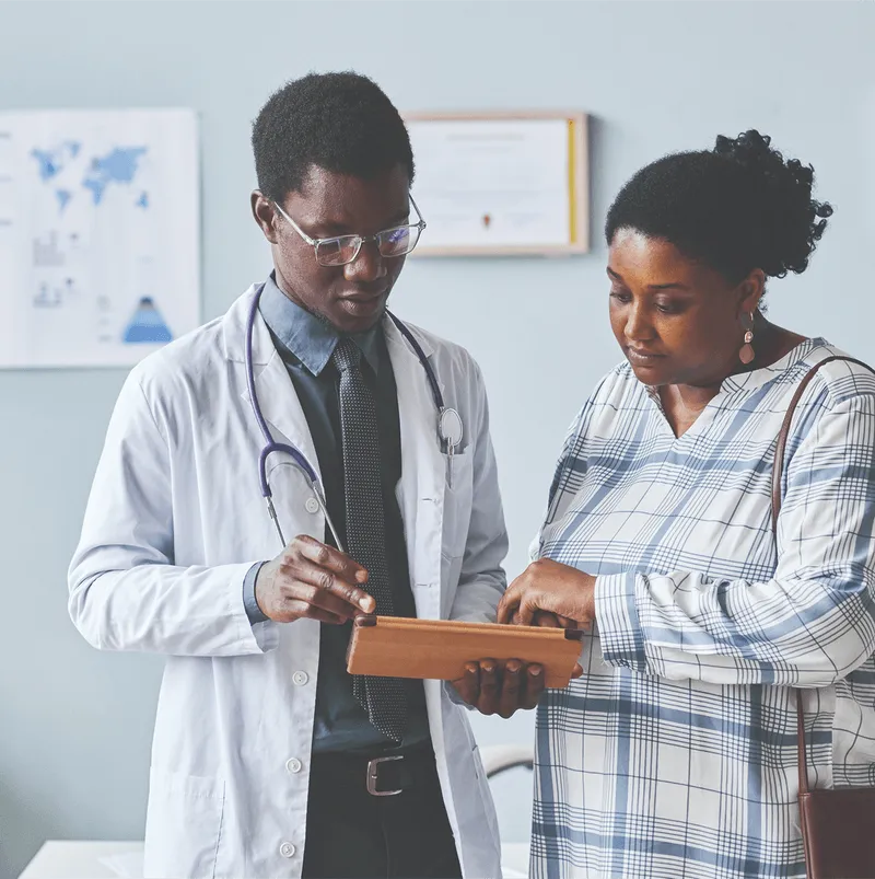 A male doctor discussing information on a tablet with a woman in a plaid dress.