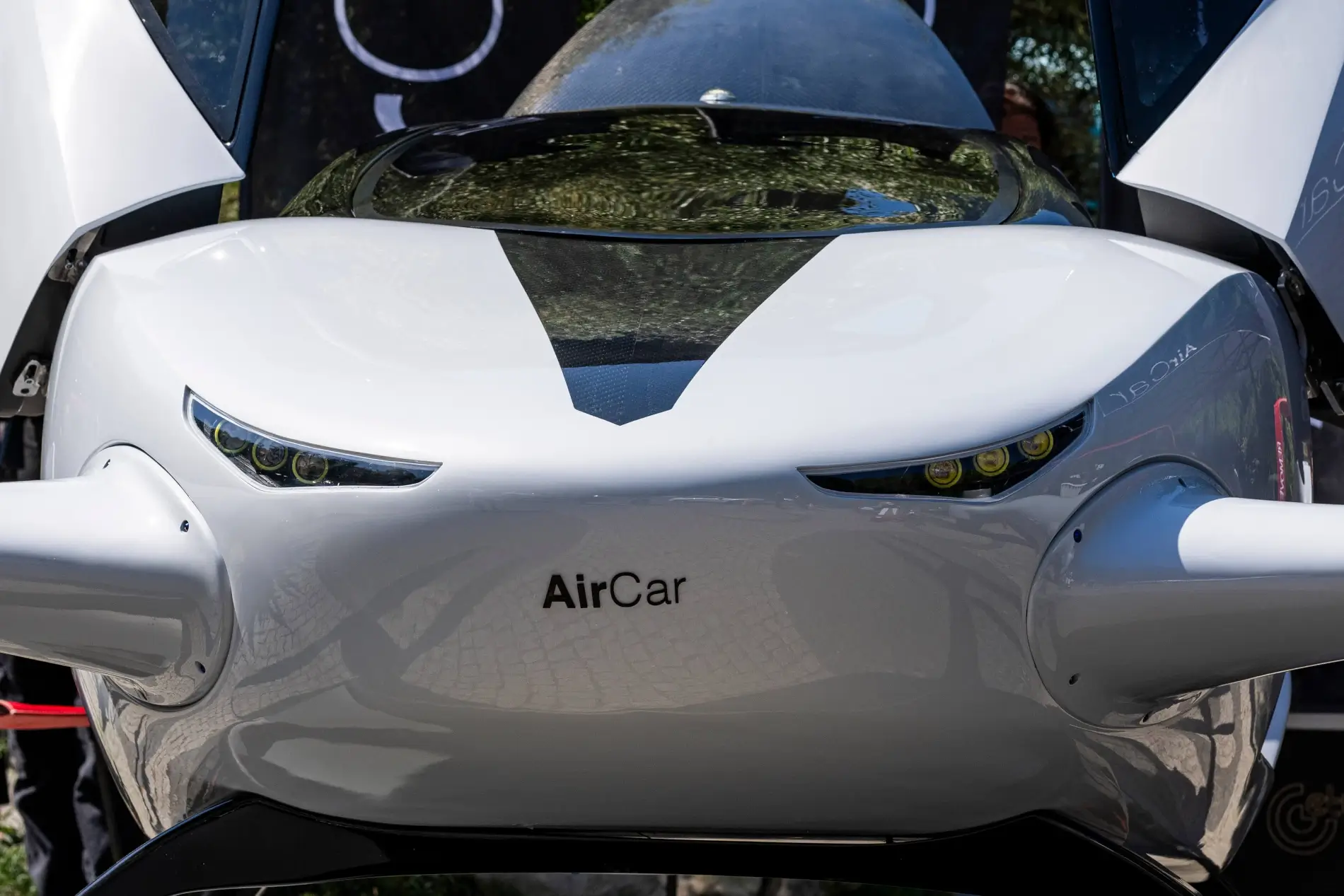 Detailní pohled na přední masku futuristického letounu AirCar s nápisem značky a úzkými LED světlomety.