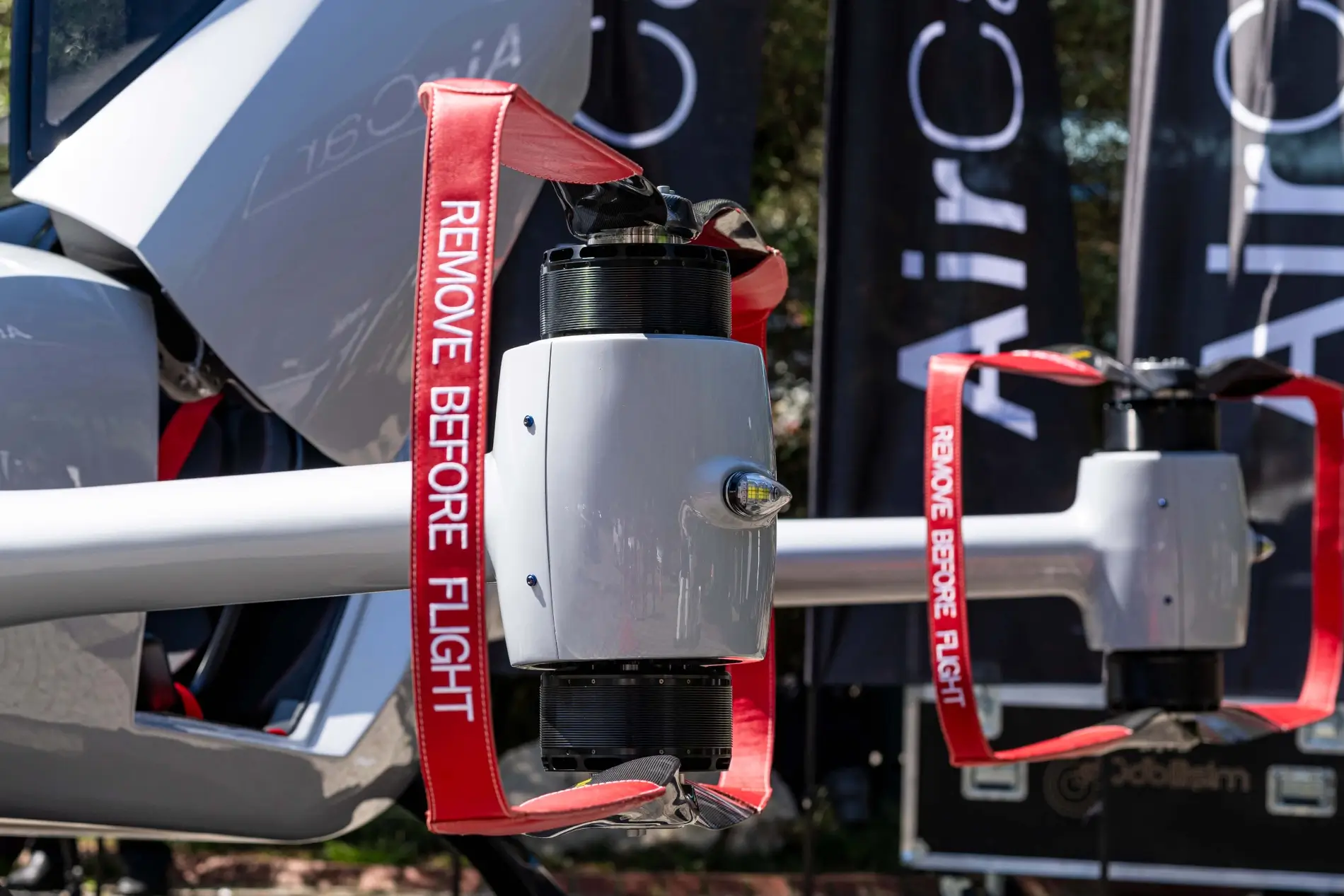 Detail ramene s elektromotorem, vrtulí a červenou bezpečnostní cedulí Remove before flight na stroji AirCar.