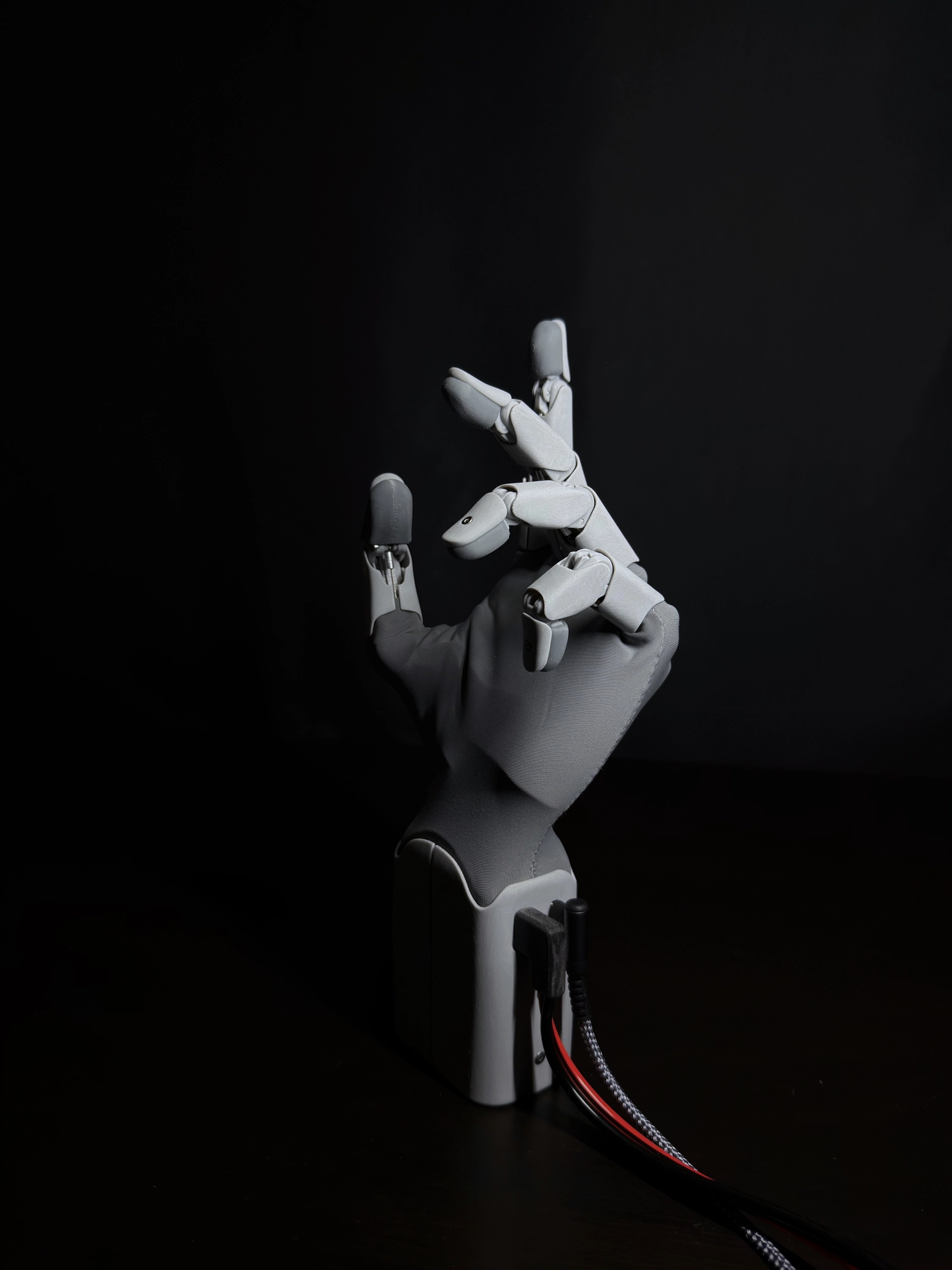 Robotická ruka HW1 z profilu v gestu částečného úchopu s kabely zapojenými do základny.