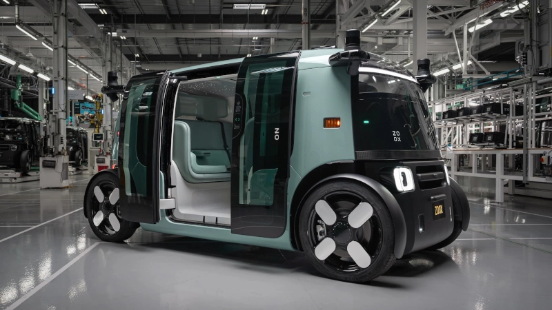 Kompletní pohled na bok robotaxi Zoox v aloe zelené barvě. Záběr v přírodní krajině zdůrazňuje jeho symetrický design, skleněné dveře a střešní senzory. Zdroj: Zoox