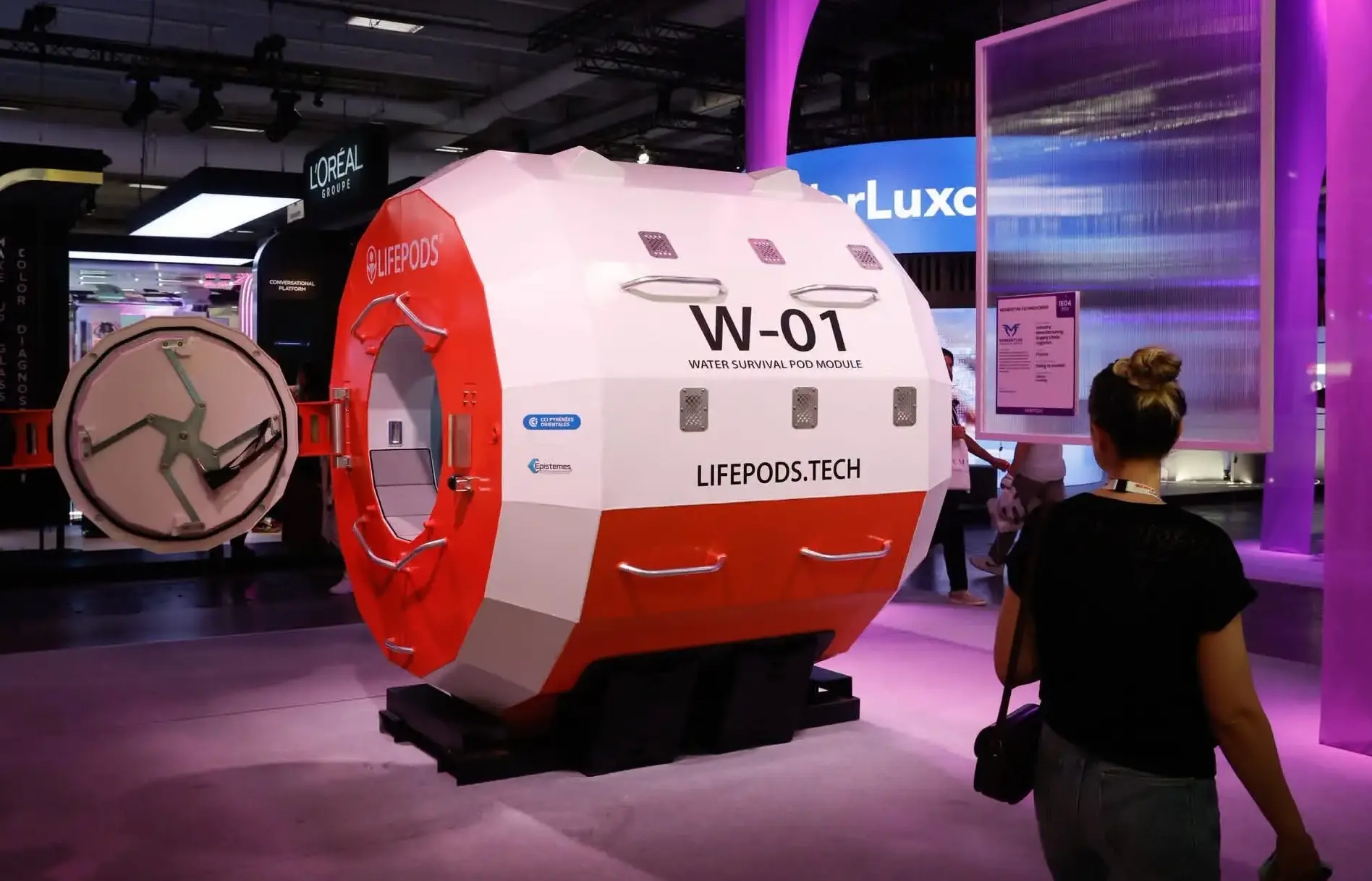 Bílo-červená plovoucí kapsle LifePods W-01 s kruhovým průlezem vystavená na veletrhu, kolem prochází návštěvnice.