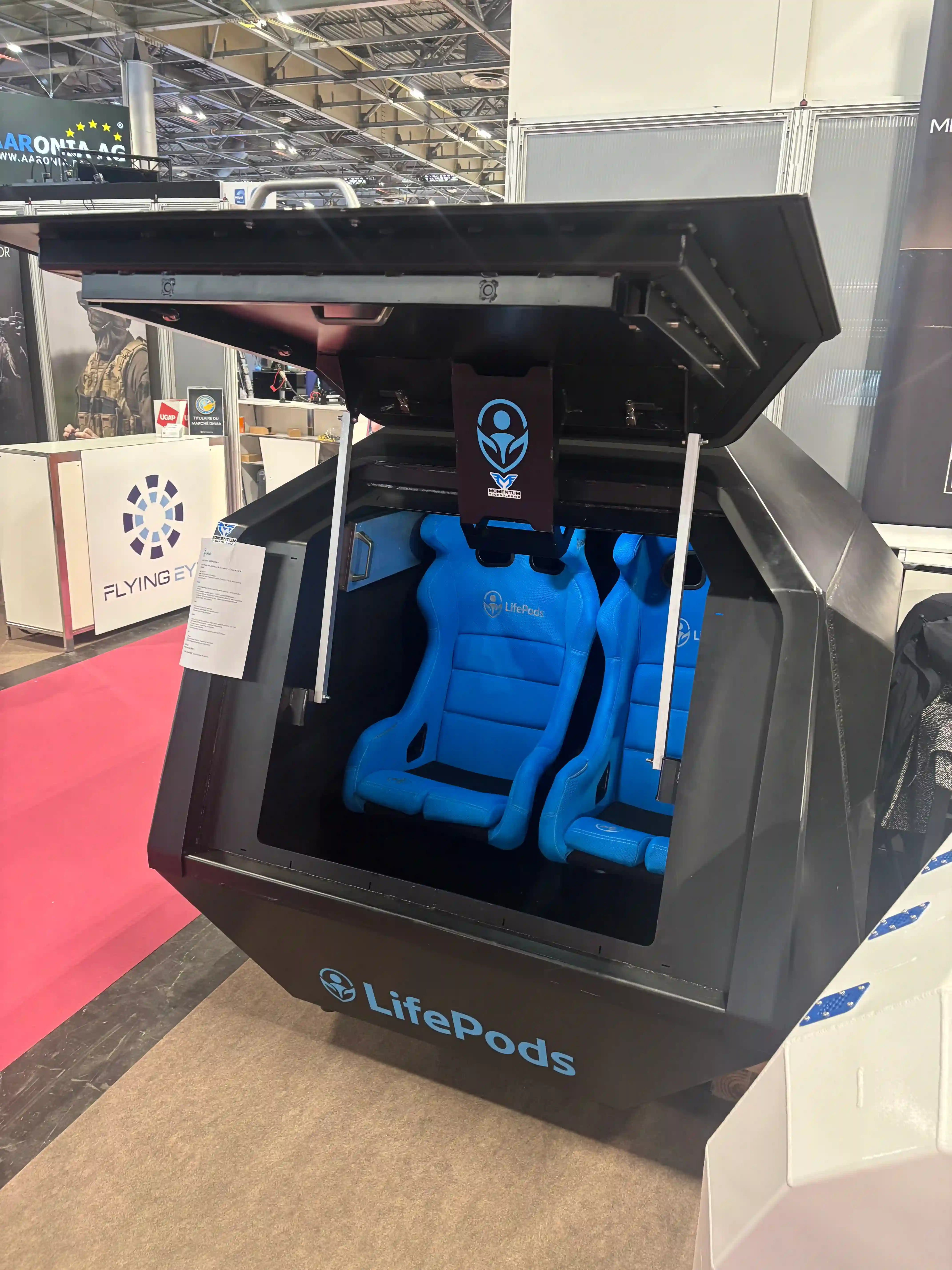 Vnitřek kapsle LifePods B-01 se dvěma modrými závodními skořepinovými sedačkami a vyklopeným ocelovým poklopem.