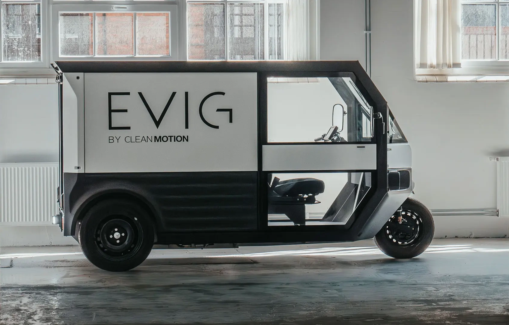 Základní bílo-černá verze doručovací solární tříkolky Clean Motion EVIG zaparkovaná v hale.