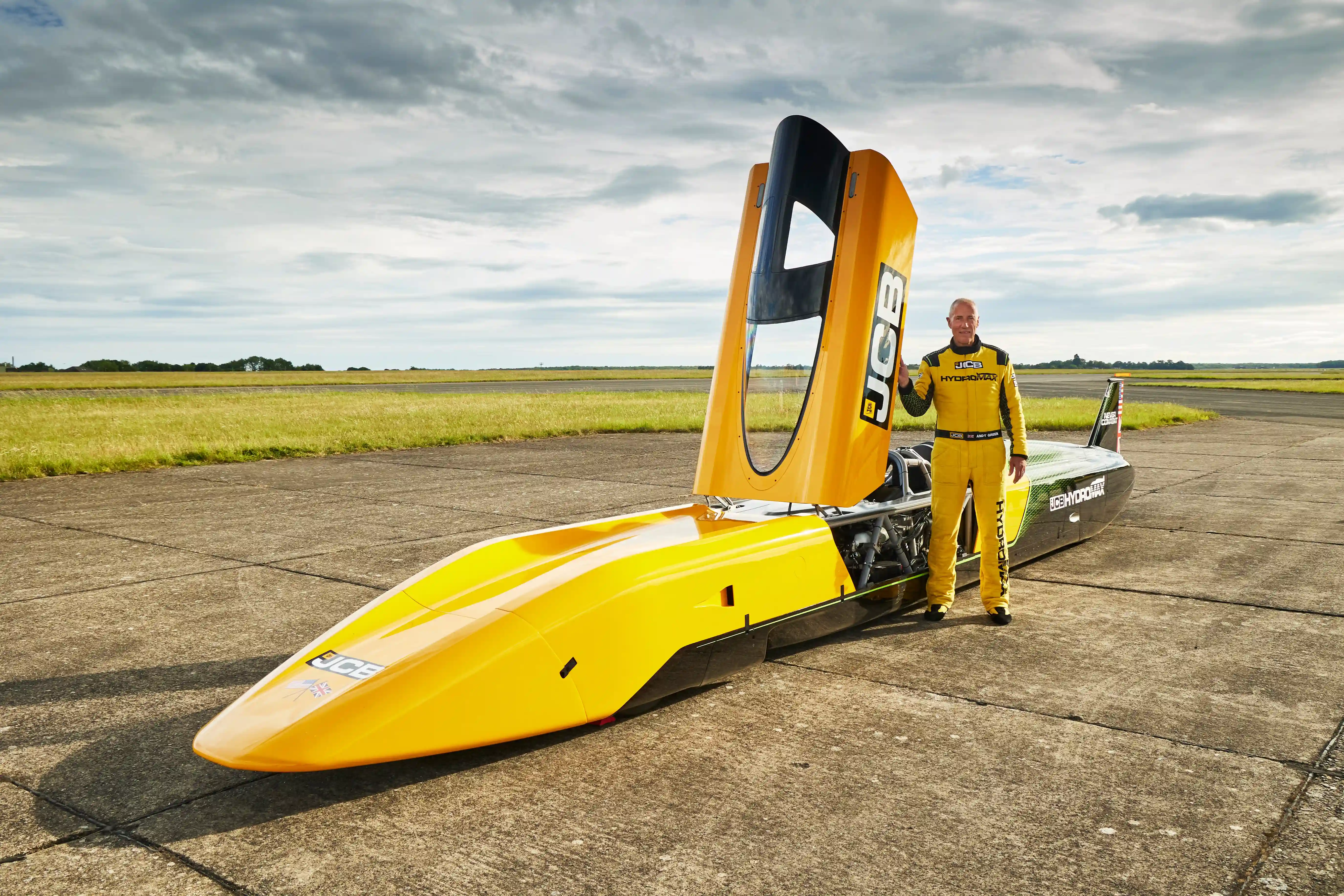Pilot Andy Green stojí vedle vodíkového vozu JCB Hydromax s otevřenými dveřmi kabiny.