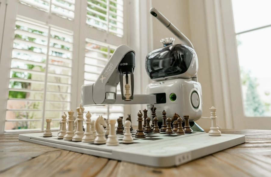 Šikmý pohled na Sense Robot manipulujícího se šachovými figurky na šachovnici.