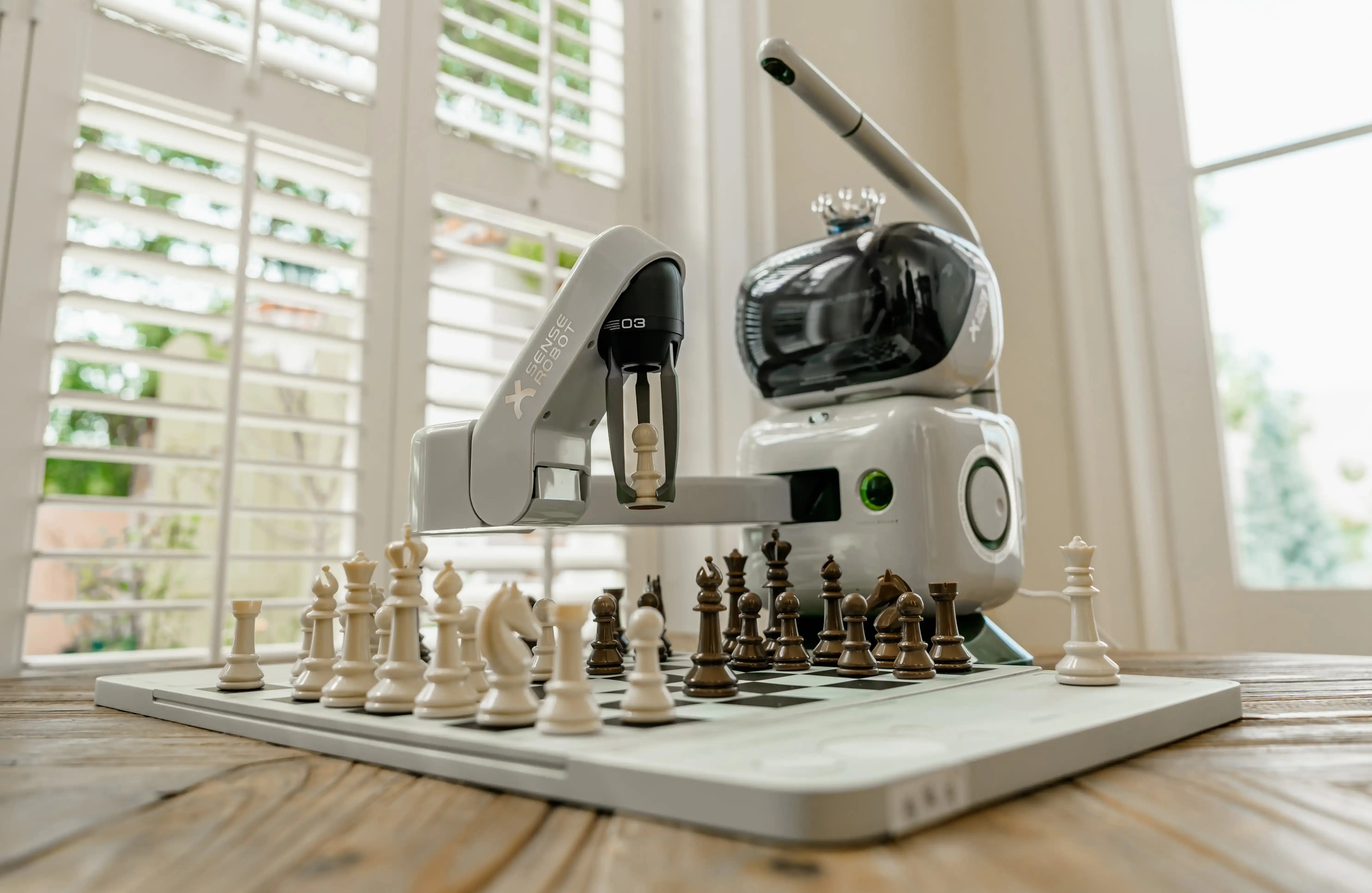 Šikmý pohled na Sense Robot manipulujícího se šachovými figurky na šachovnici.