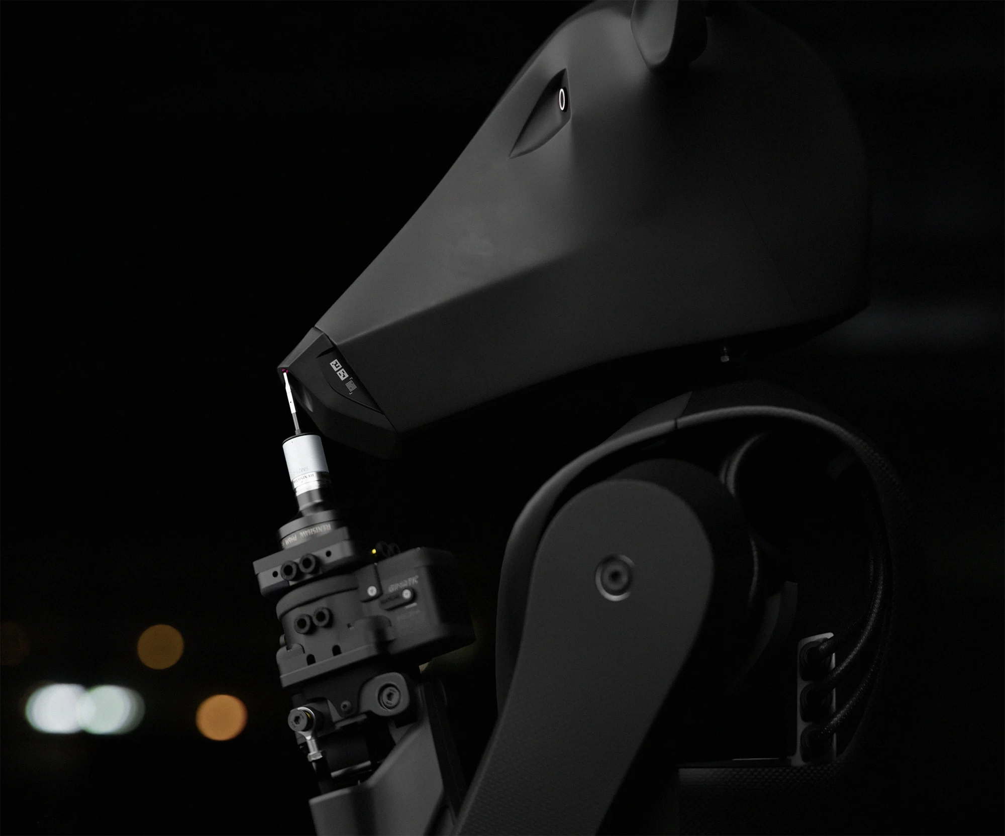 Robot Threehalves drží v zápěstní rychlospojce měřicí sondu, detail kozlí hlavy a paže v tmavé hale.
