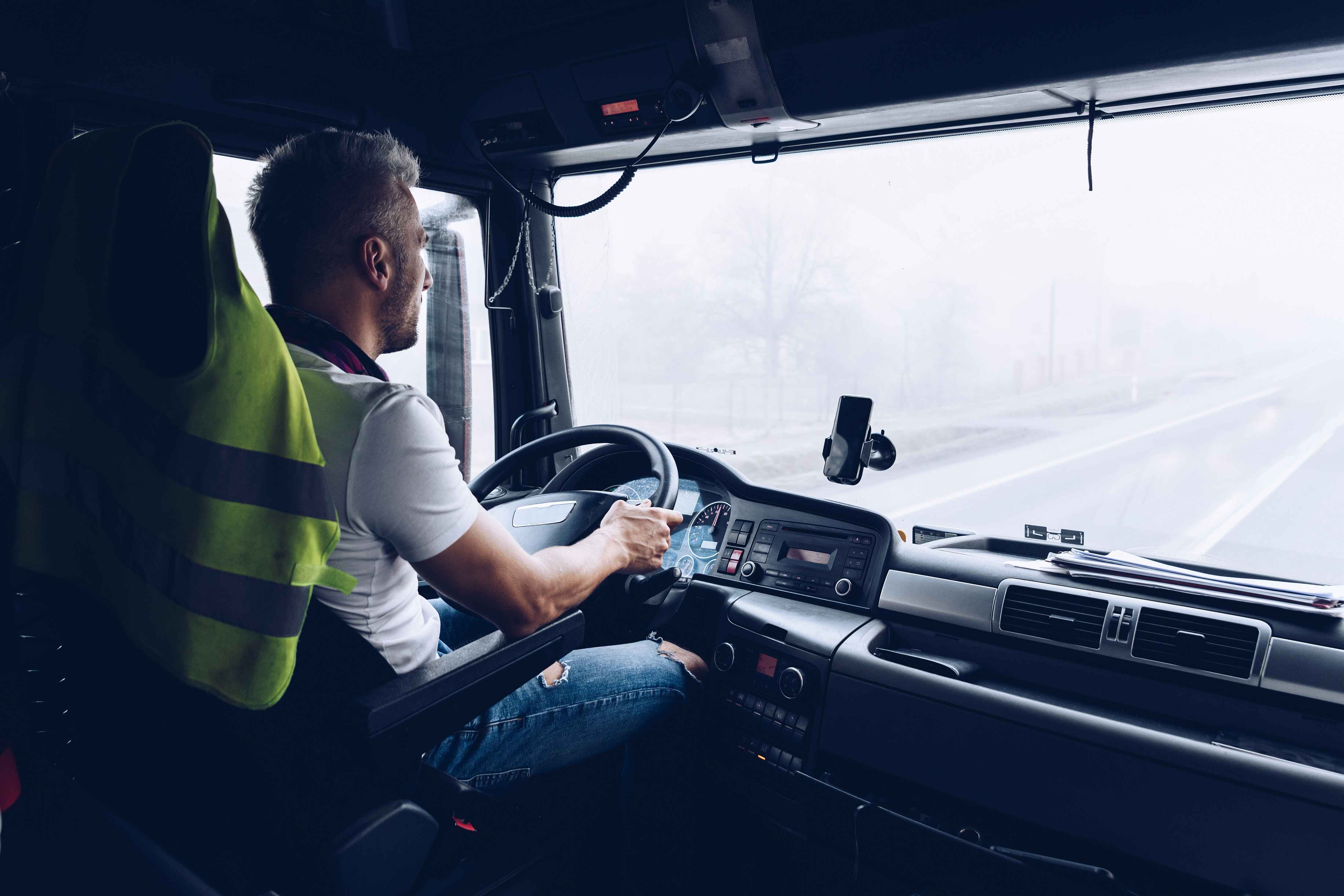 Professional truck driver navigating through foggy road conditions, wearing a high-visibility safety vest, representing Egala company’s commitment to safe and reliable transportation services.