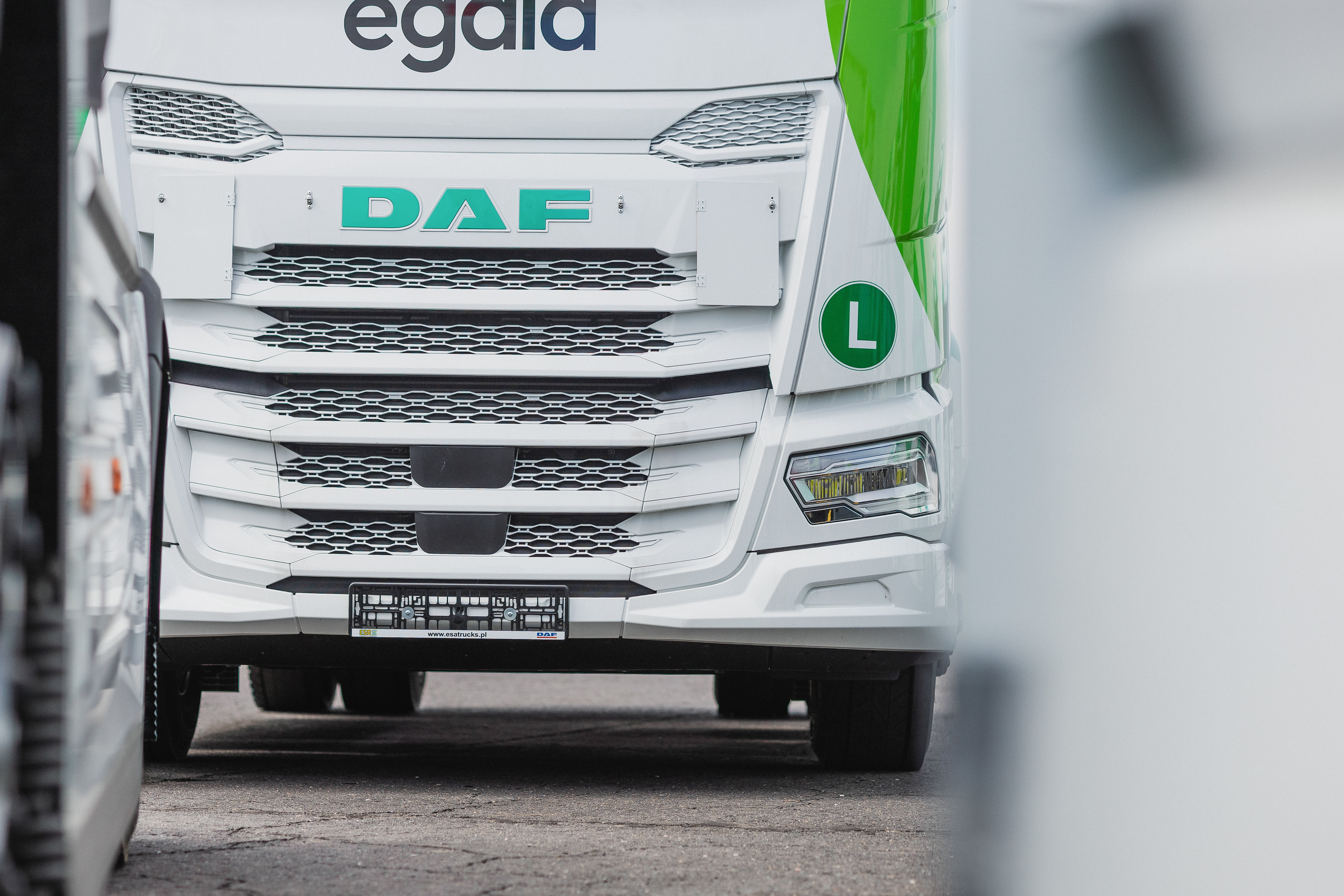 Front view of an Egala-branded DAF semi-truck driving between other trucks on a road, featuring green accents and an L learner driver sign on the cab.