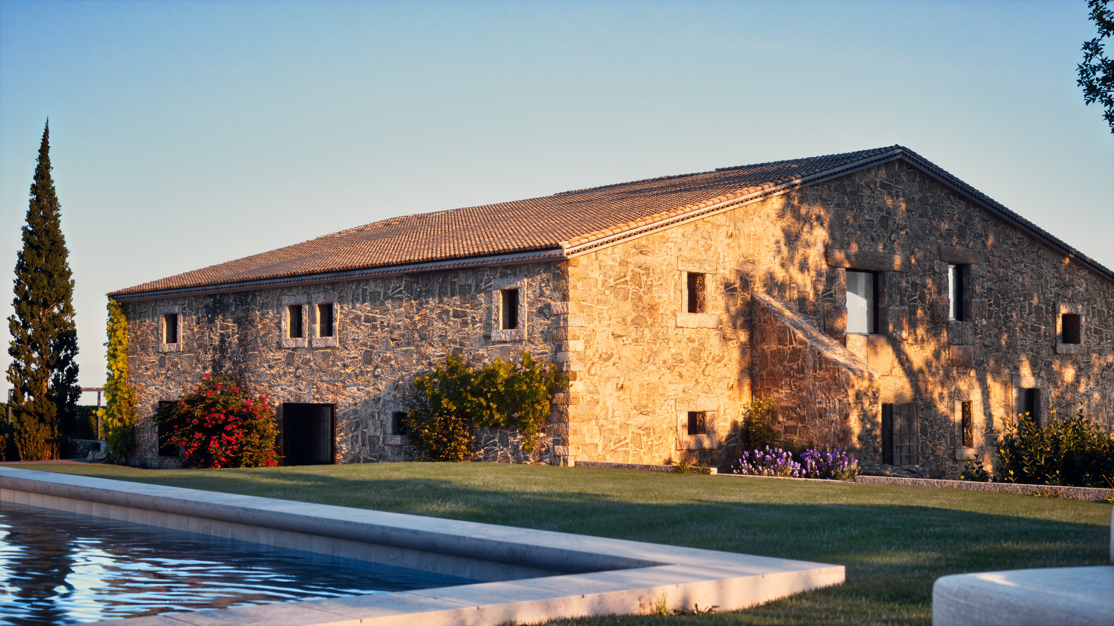Stone house view with pool foreground and evening sunlight.
