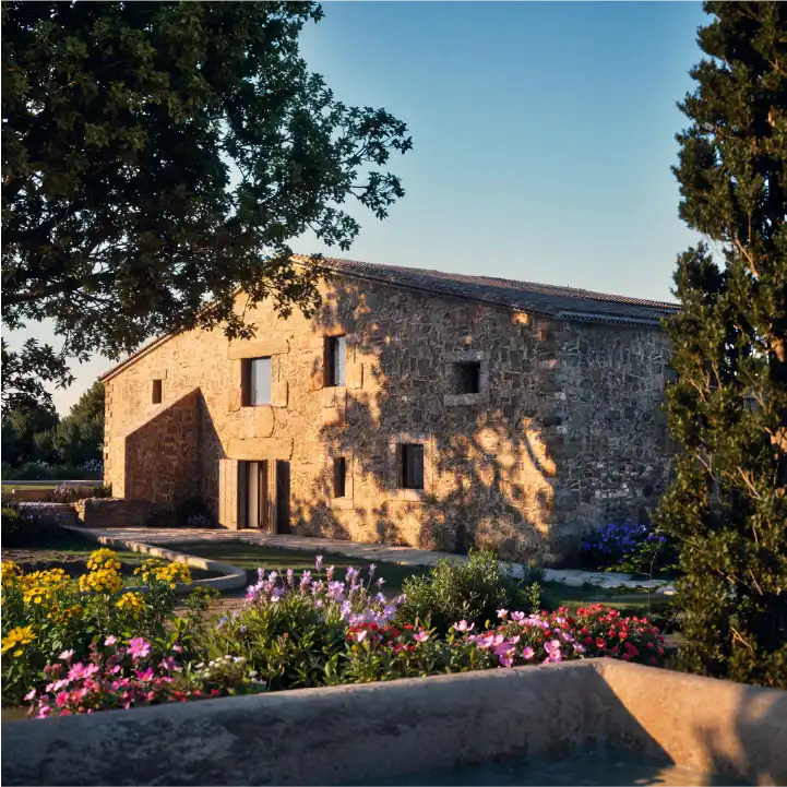Stone house view with pool foreground and evening sunlight.