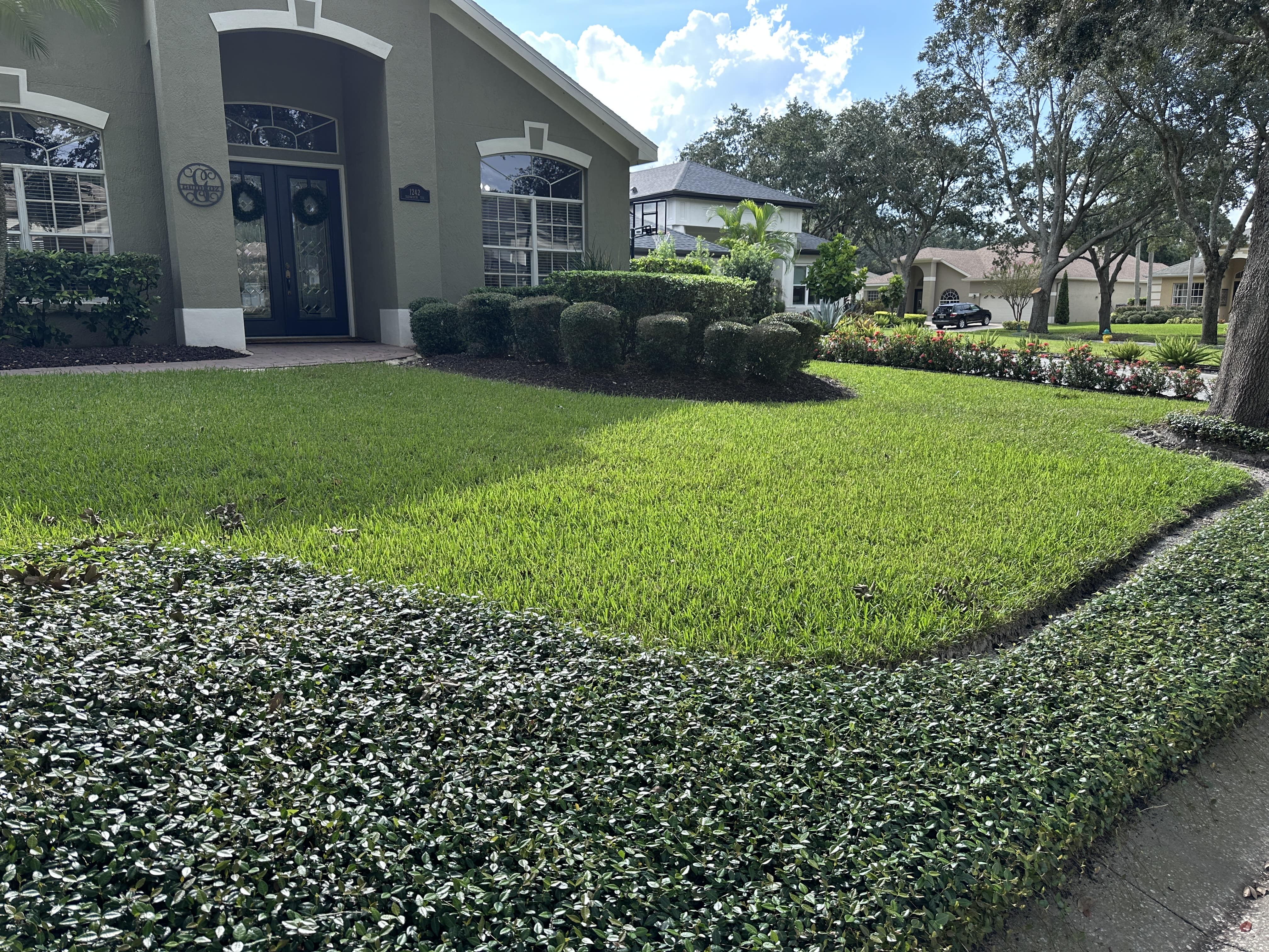 Well-maintained front yard with green lawn, trimmed bushes, and a house entrance with double dark doors.