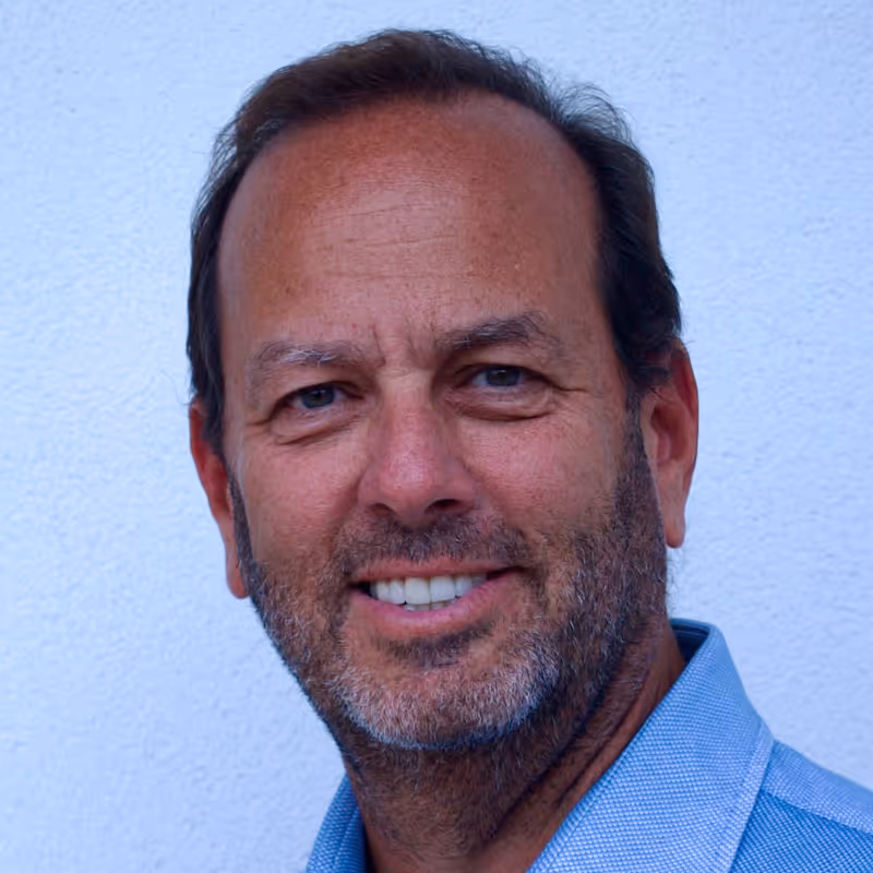 Middle-aged man with beard smiling in blue collared shirt