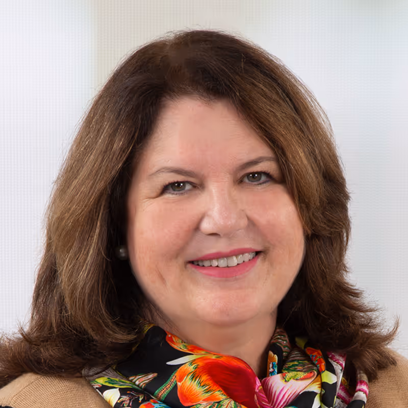 Woman with brown hair smiling, wearing colorful floral scarf