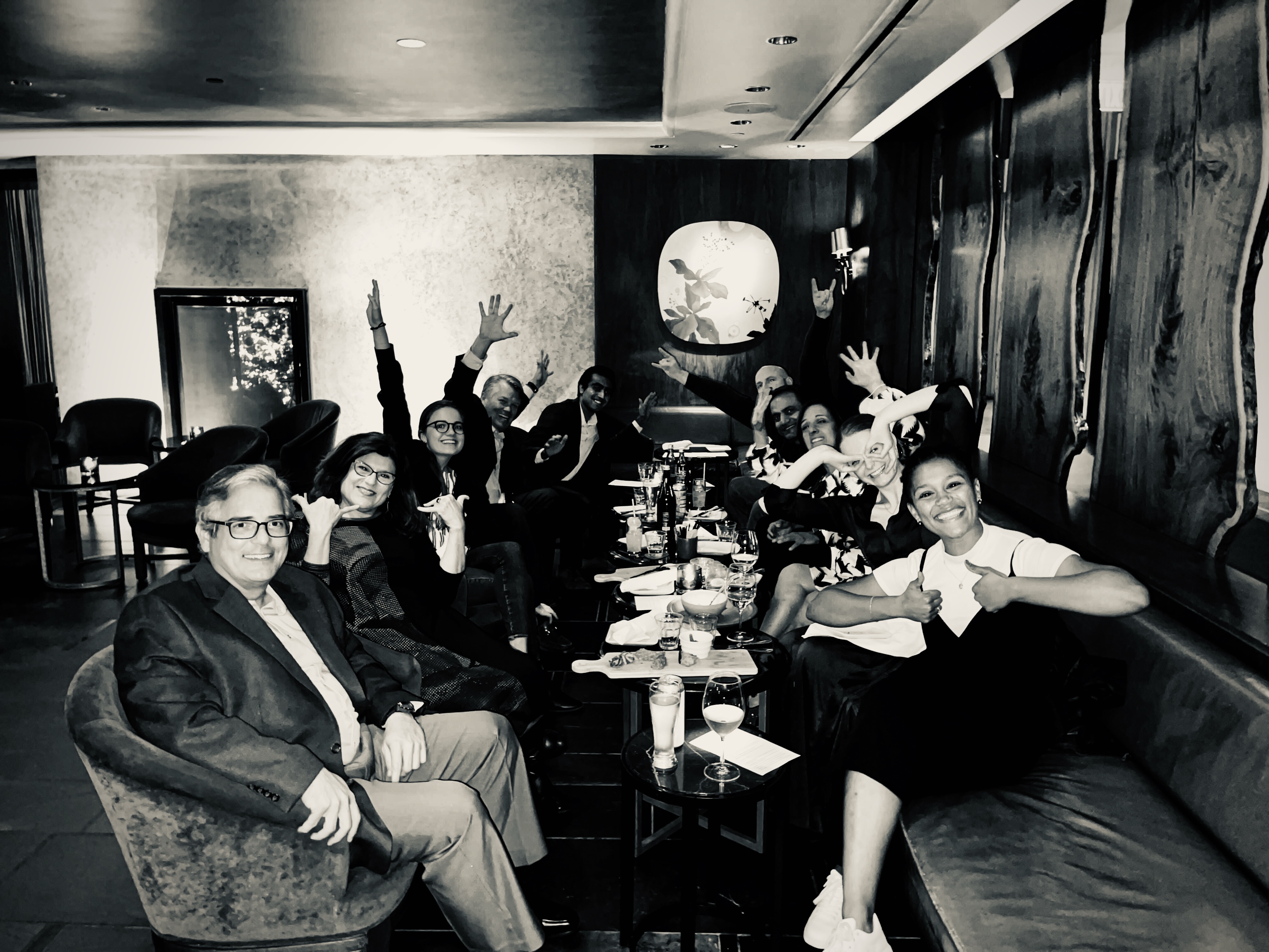 Joyful group celebrating at a table with raised hands and drinks