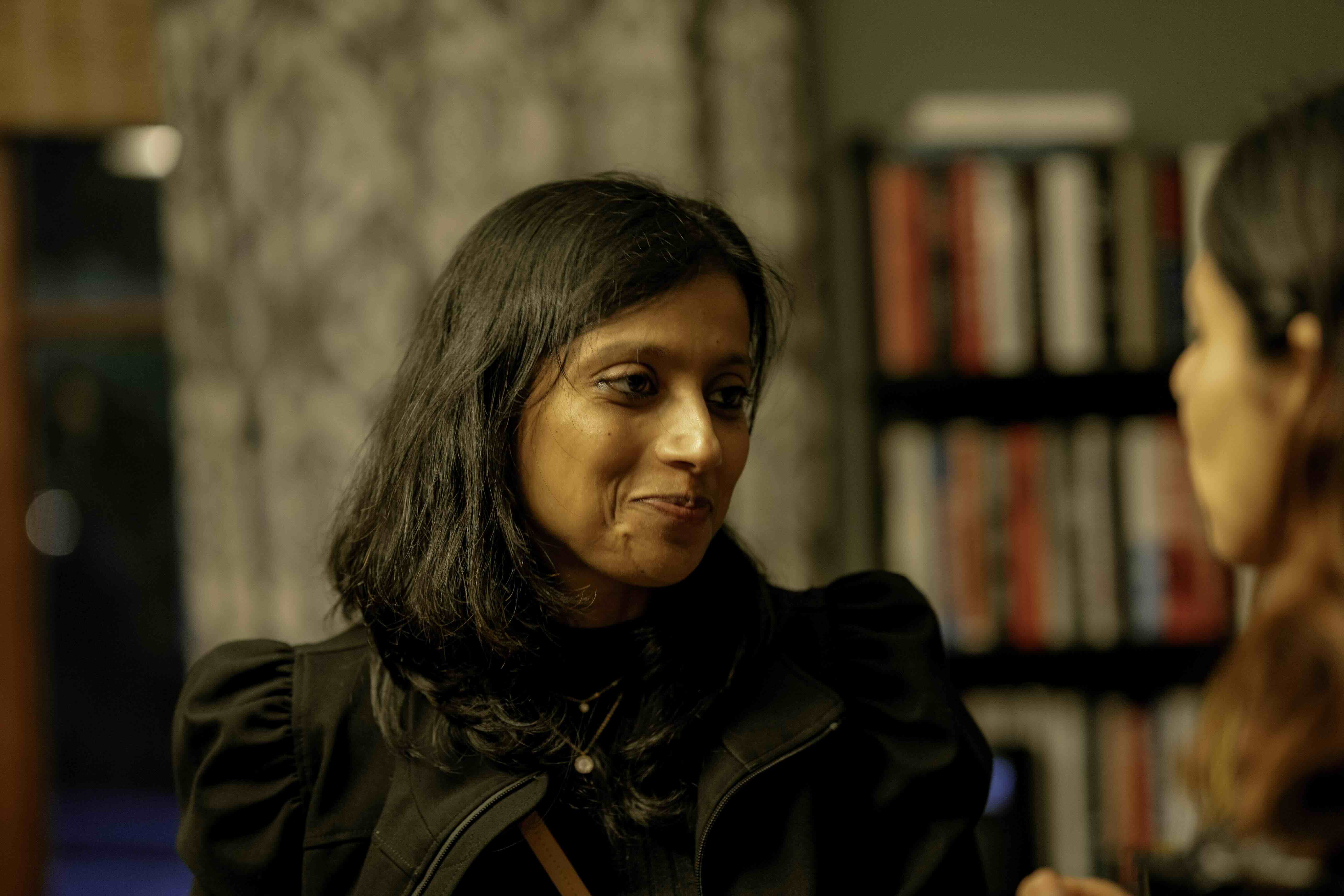 Woman in black jacket smiling in library with bookshelves behind her