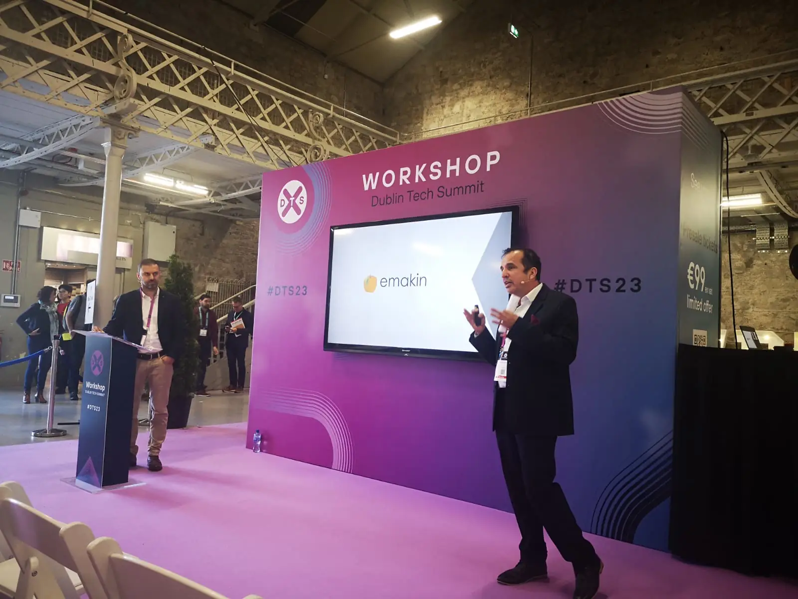 Speaker presenting on stage at the Dublin Tech Summit workshop with a screen displaying the Emakin logo.