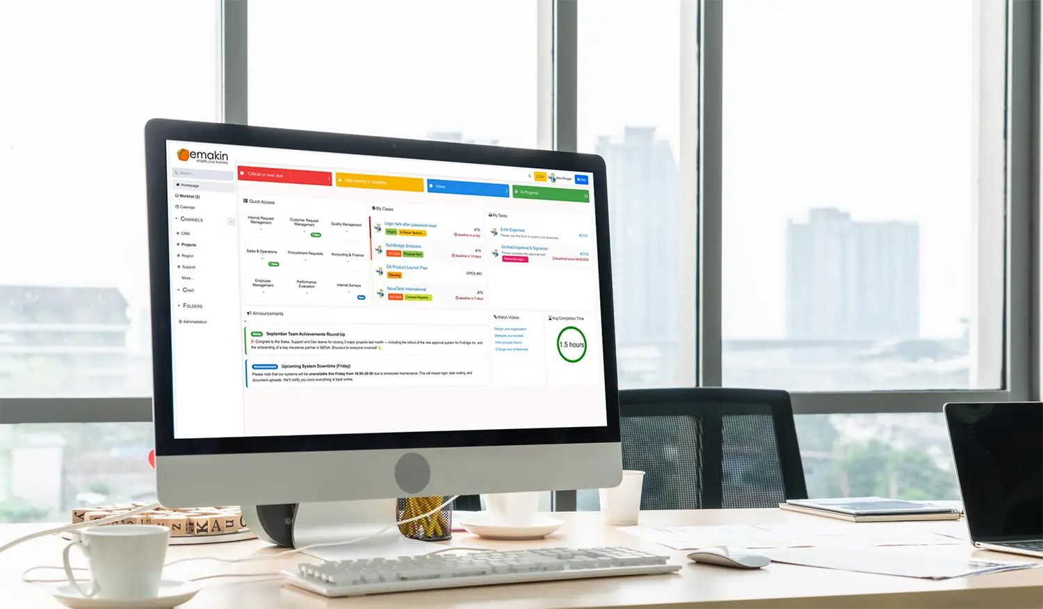 Computer on desk displaying Emakin business management software dashboard in a bright office with city view.