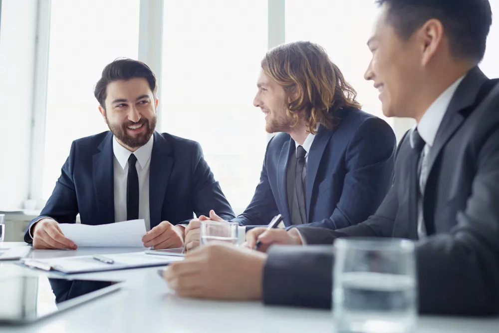 Three professionals in a meeting discussing charts and documents at a white table.