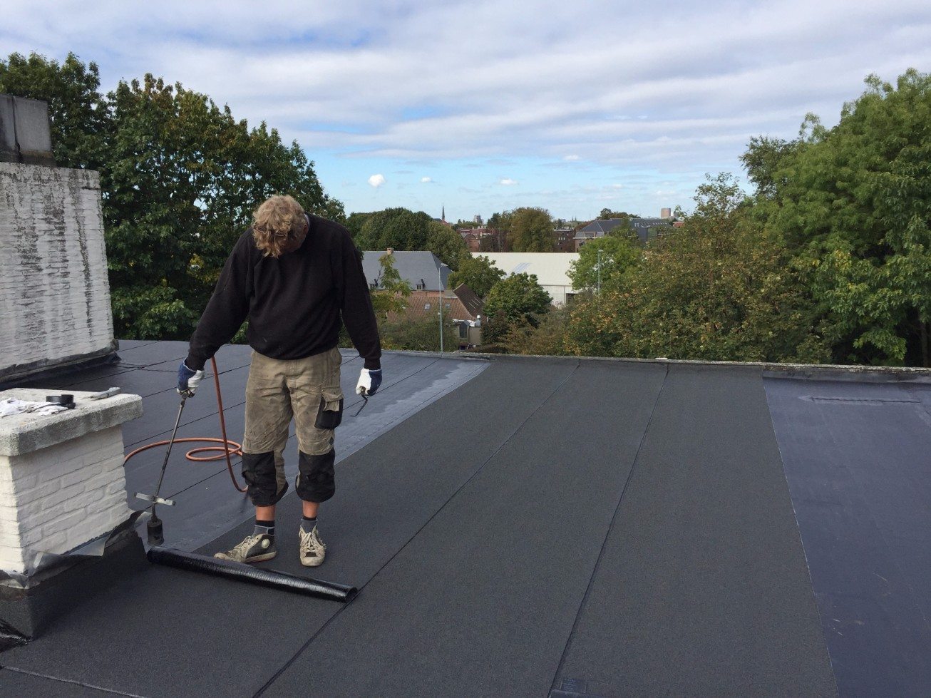 Een dakdekker brand een toplaag op een onderlaag van een roofingdak