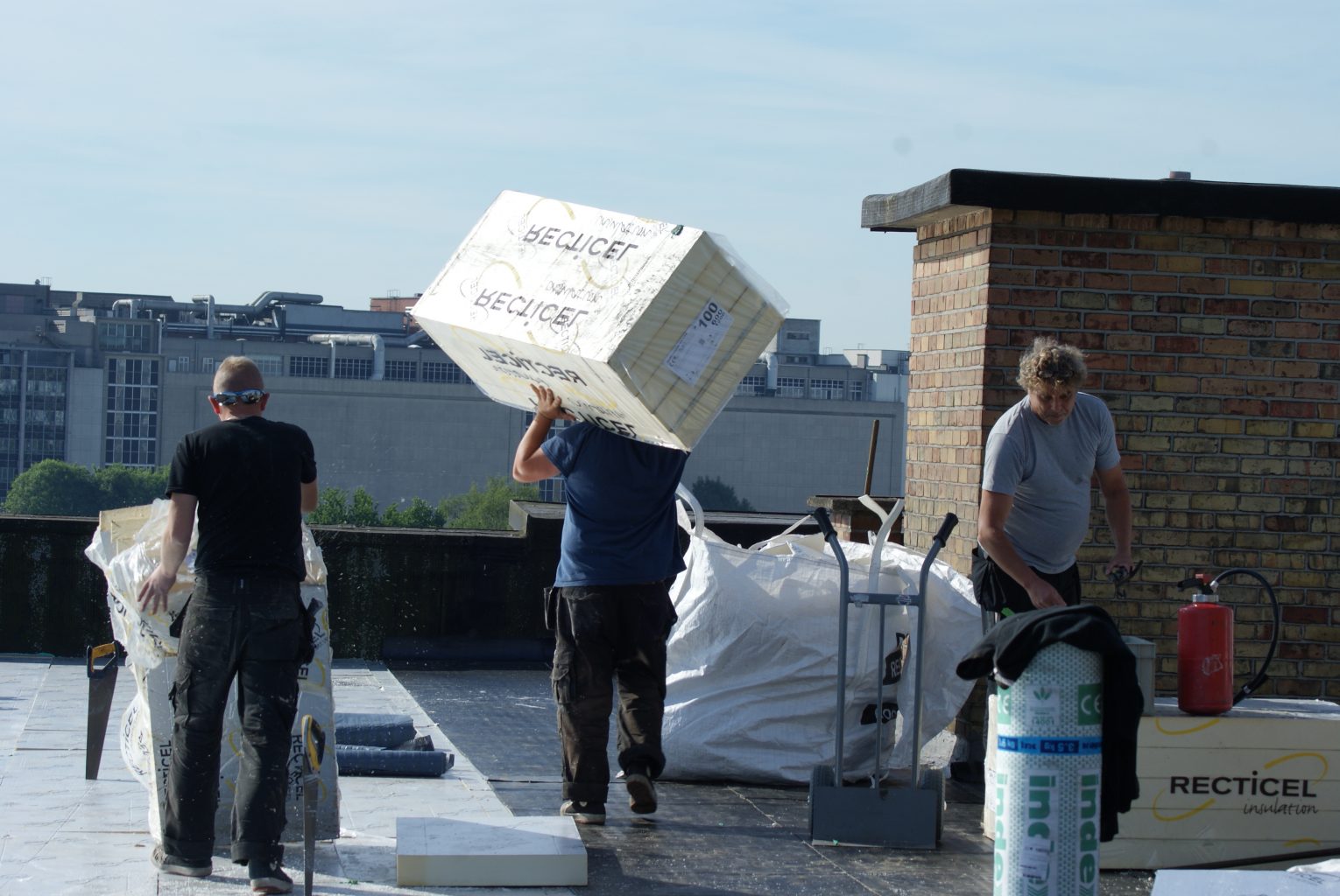 3 dakdekkers in beeld op een werf. Een dakdekker draagt allemaal roofing op zijn schouder