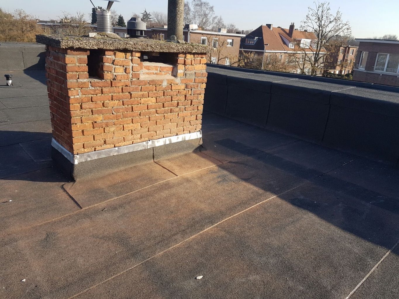 Een foto van een afgewerkt roofingdak met focus op een afwerking rond de schoorsteen