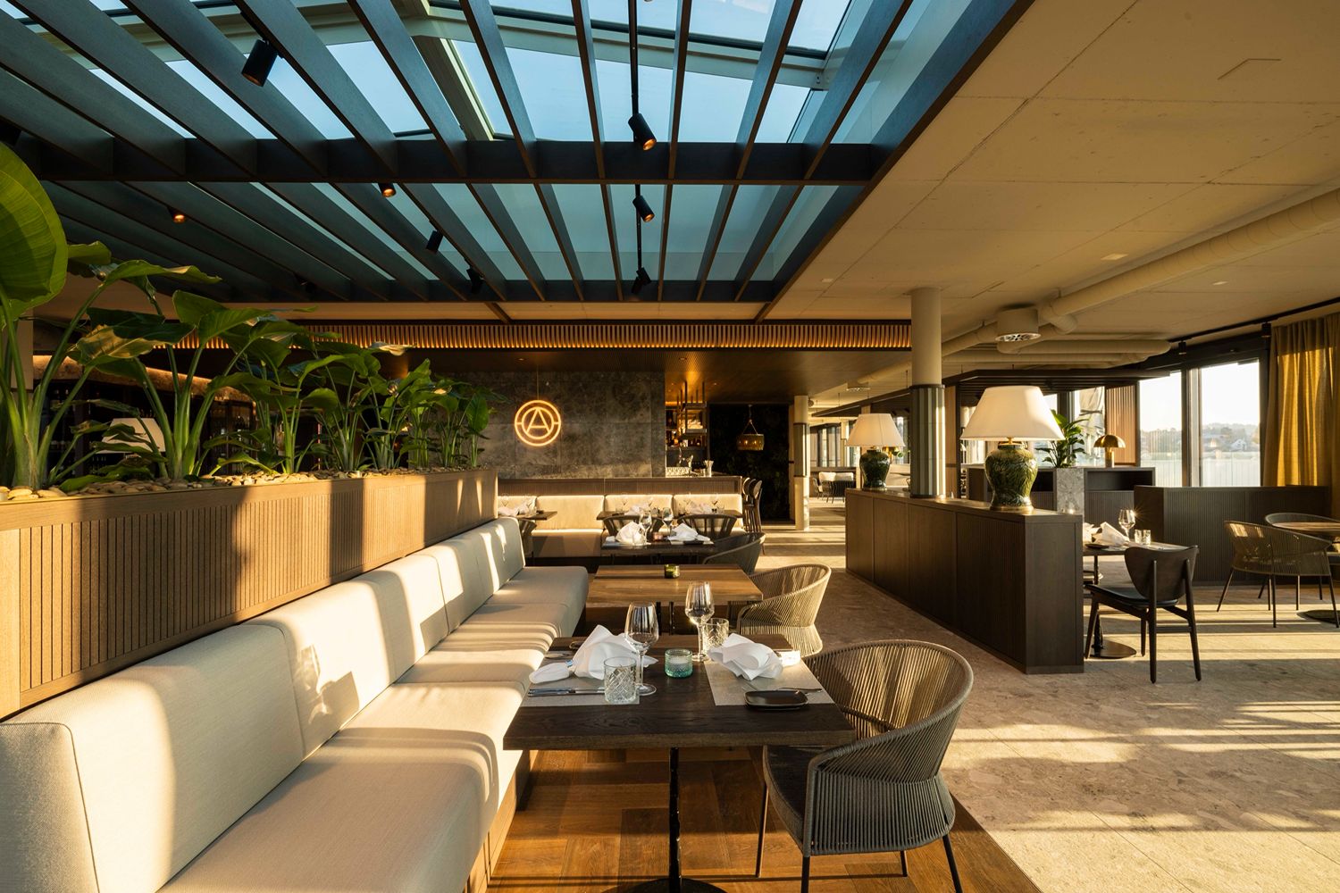 Modernes Restaurant-Interieur mit Pflanzen, Tischen, Stühlen und bequemen Sitzgelegenheiten für ein kulinarisches Erlebnis.
